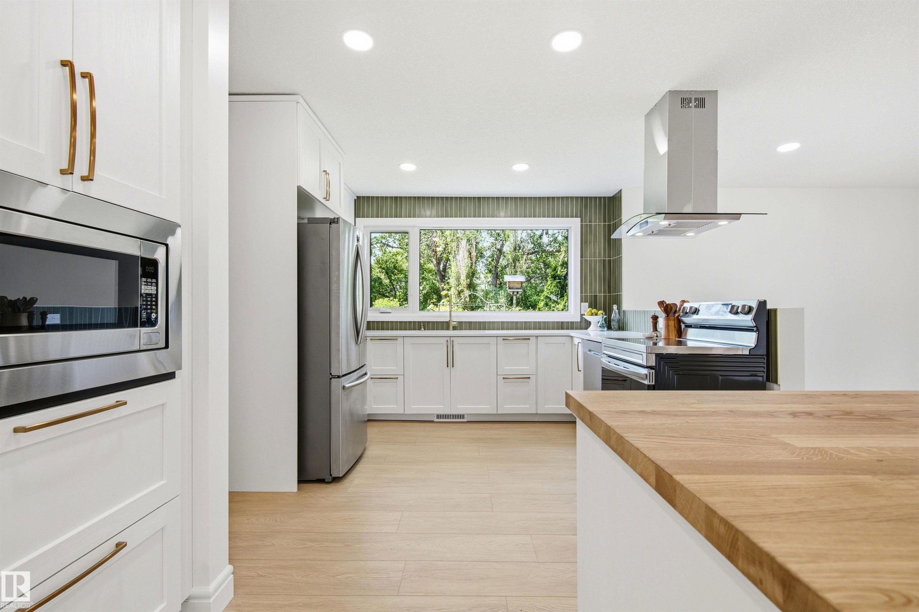 Modern kitchen featuring white cabinetry, stainless steel appliances, wood-finish flooring, recessed lighting, and a green tile backsplash - 14335 47 Avenue Nw, Edmonton, AB - Indoor Photo Showing Kitchen