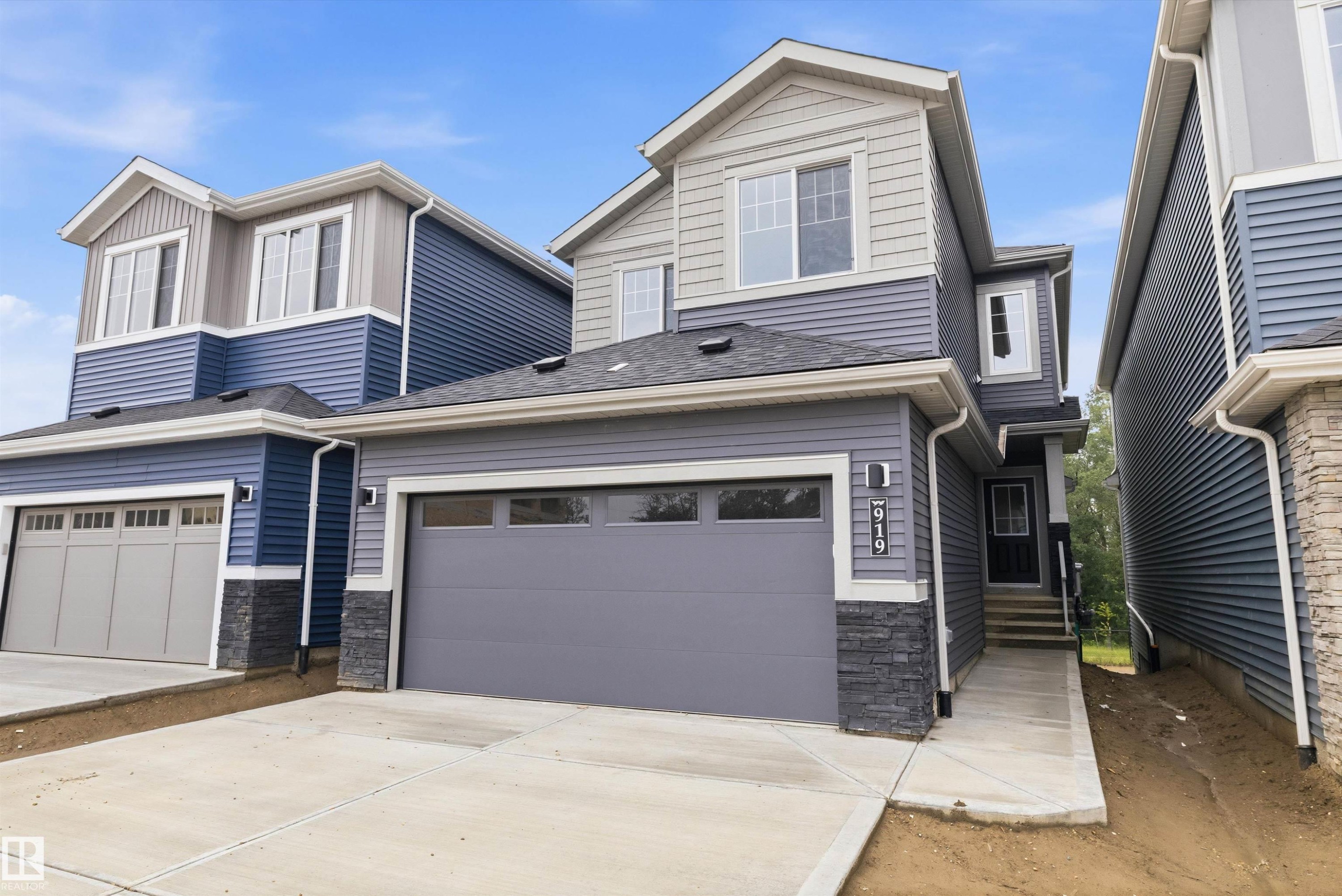 Contemporary two-story residence featuring multi-toned siding, an integrated single-car garage, stone accents on the facade, and a covered entry with steps - 919 Elderberry Landing Nw, Edmonton, AB - Outdoor With Facade