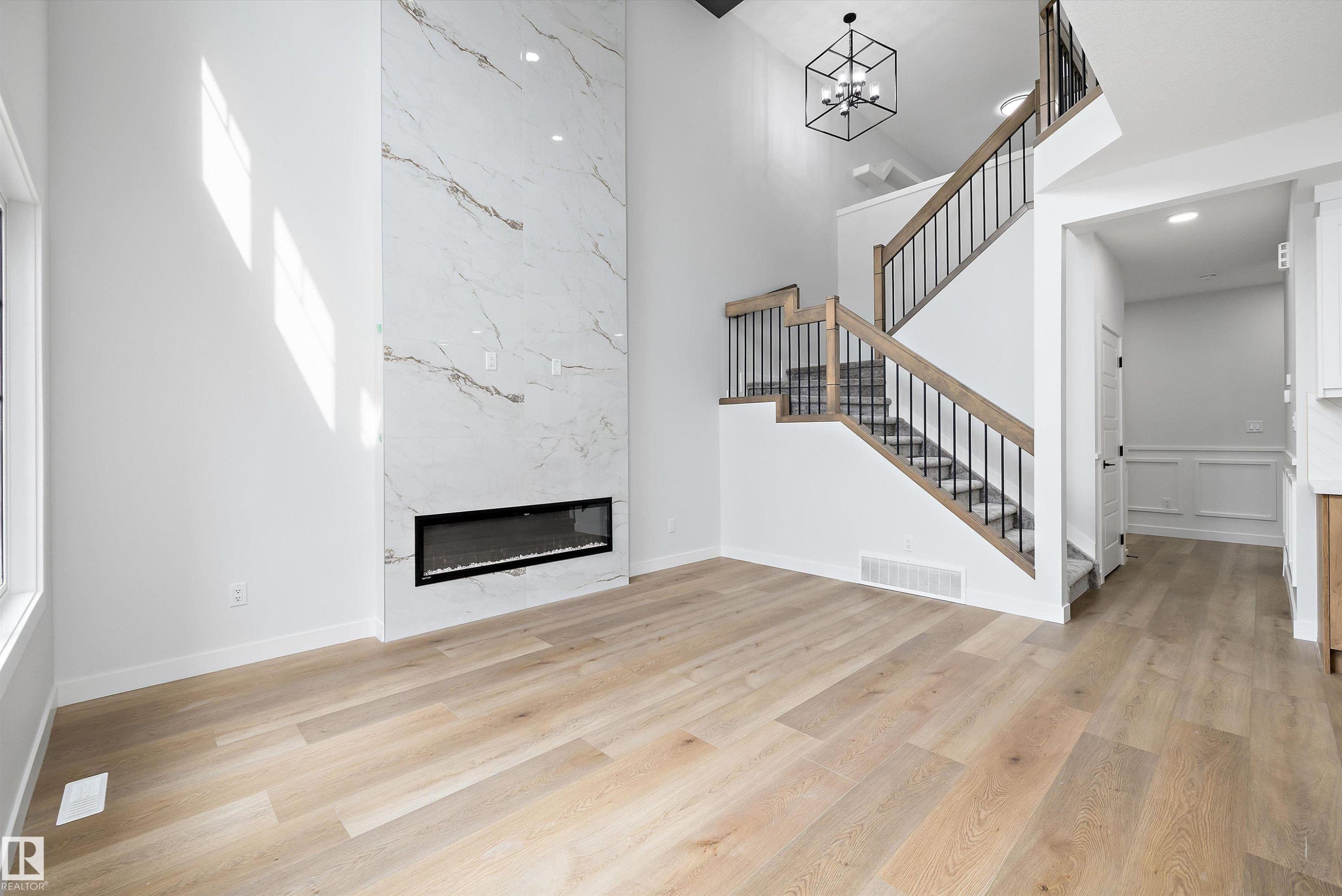 Soaring ceilings complement the full-height fireplace featuring a linear electric insert and large format porcelain tile - 919 Elderberry Landing Nw, Edmonton, AB - Indoor With Fireplace