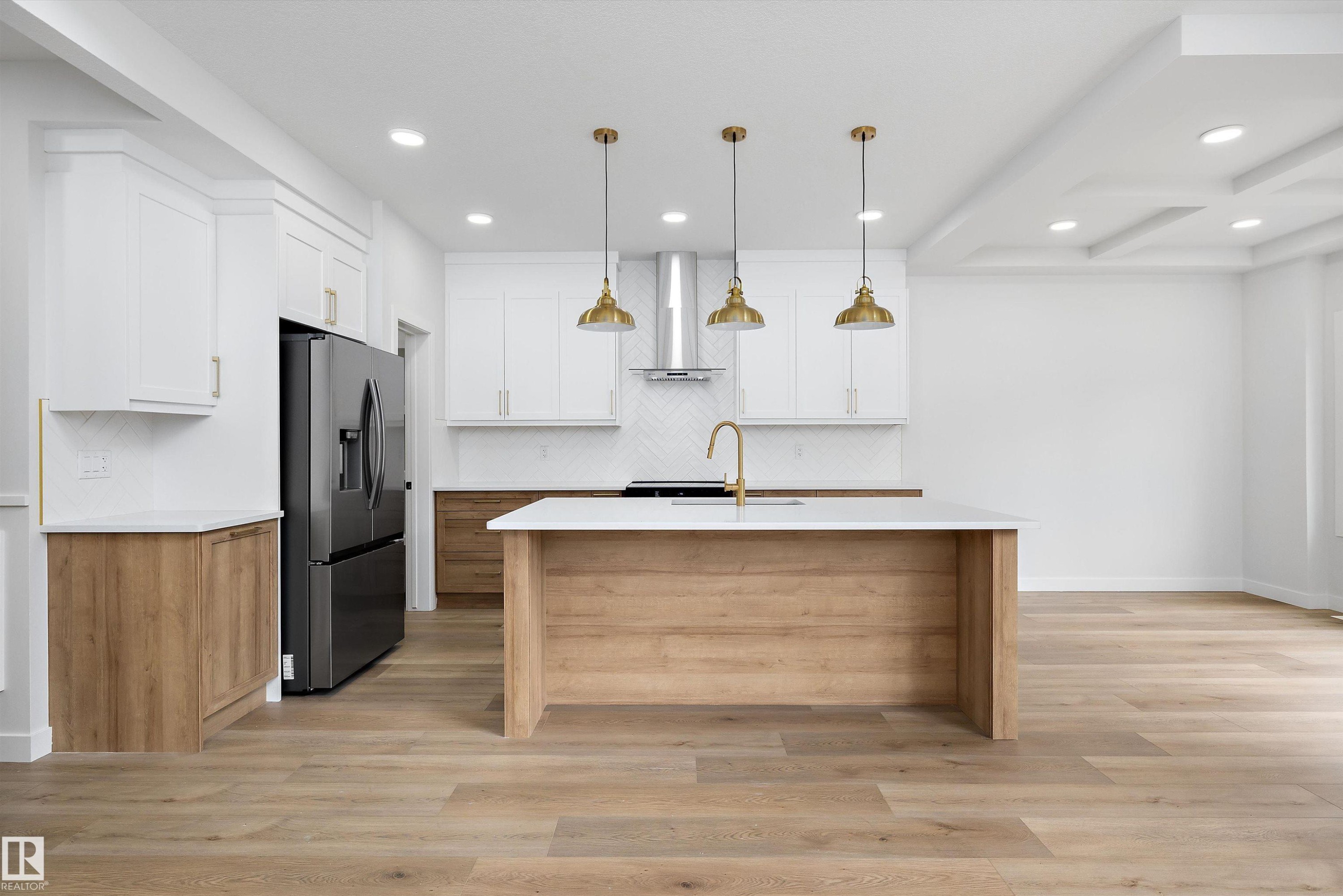 Contemporary kitchen featuring a large central island, white shaker cabinetry, wood-finish lower cabinetry, a herringbone tile backsplash, and recessed lighting - 919 Elderberry Landing Nw, Edmonton, AB - Indoor Photo Showing Kitchen With Upgraded Kitchen