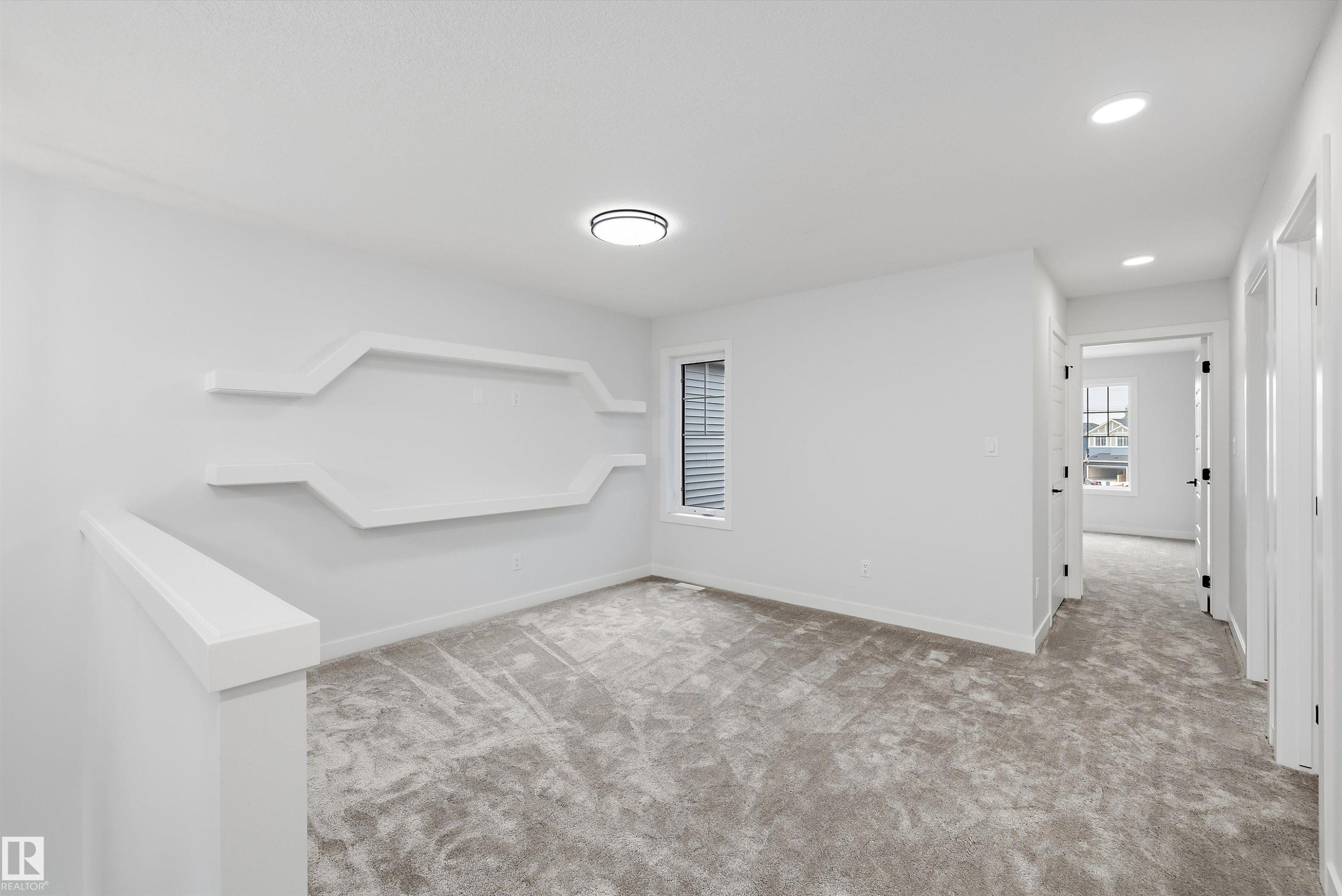 Carpeted landing area featuring a decorative architectural wall with integrated shelving, a large window with blinds, recessed lighting, and a contemporary flush-mount light fixture - 919 Elderberry Landing Nw, Edmonton, AB - Indoor Photo Showing Other Room