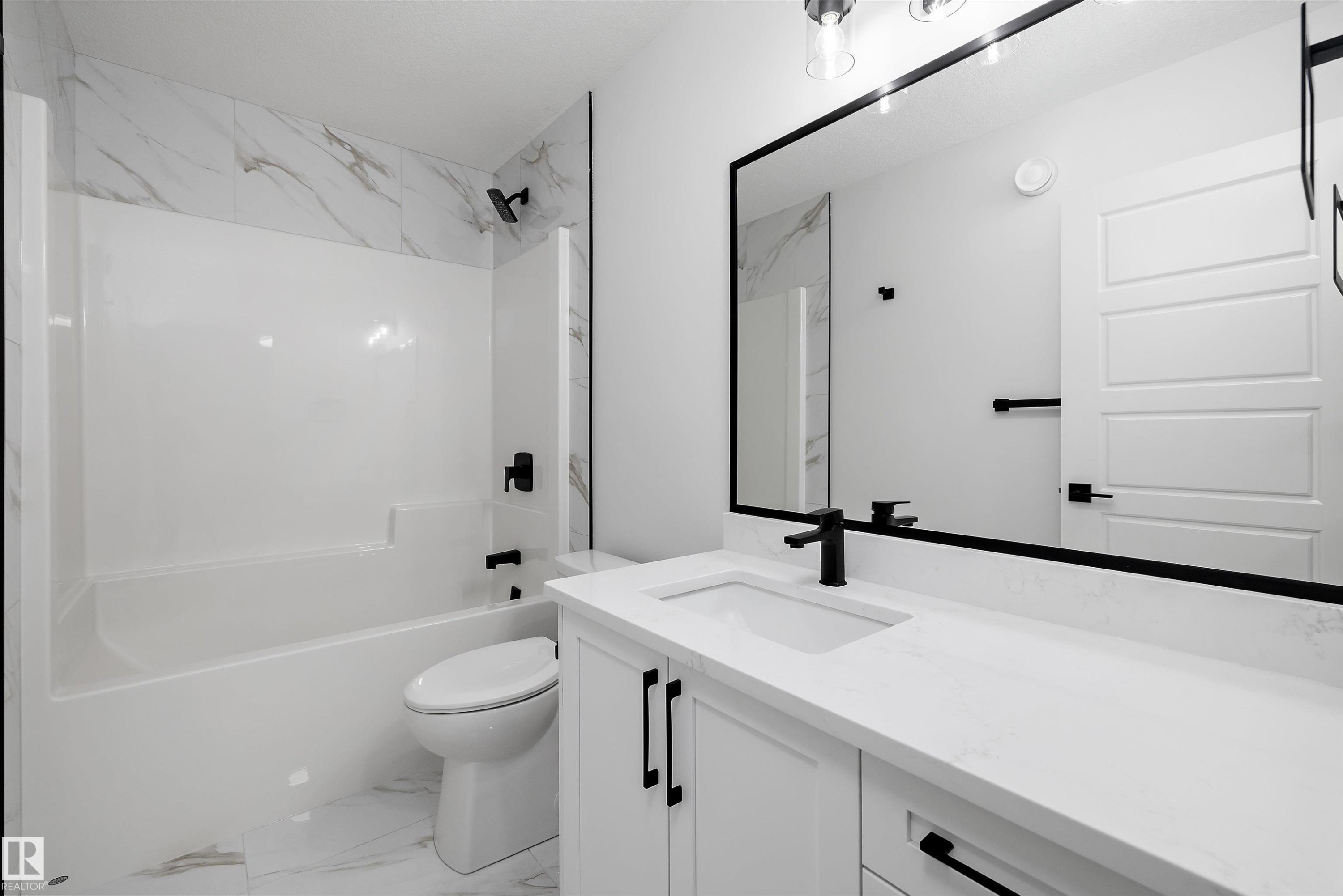 Contemporary bathroom featuring a white tub/shower combination with a marble-look tile surround, a white vanity with a rectangular undermount sink, a large framed mirror, and matte black fixtures - 919 Elderberry Landing Nw, Edmonton, AB - Indoor Photo Showing Bathroom