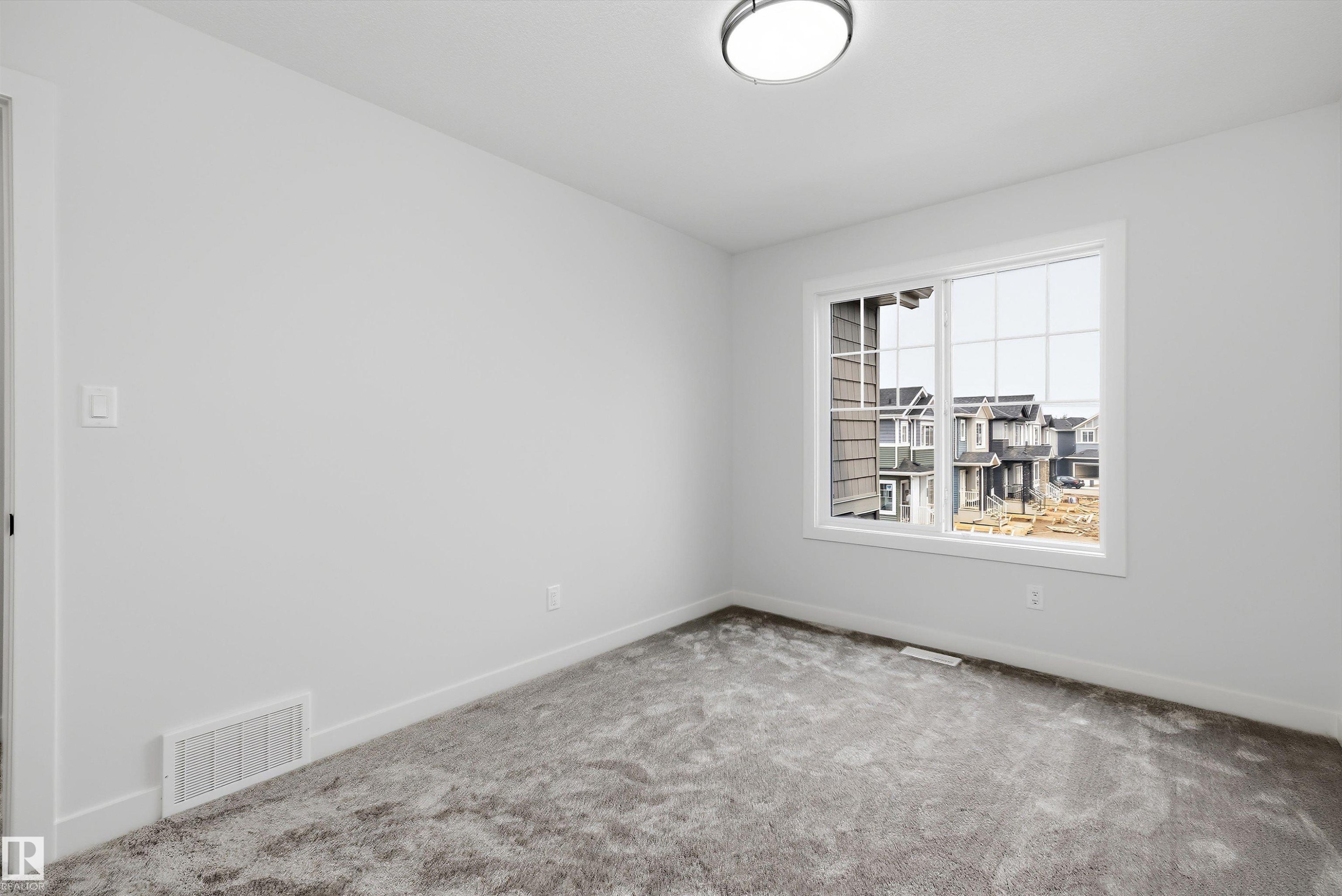 Neutral-toned room featuring a large window, light gray walls, dark gray patterned carpeting, and white baseboards - 919 Elderberry Landing Nw, Edmonton, AB - Indoor Photo Showing Other Room
