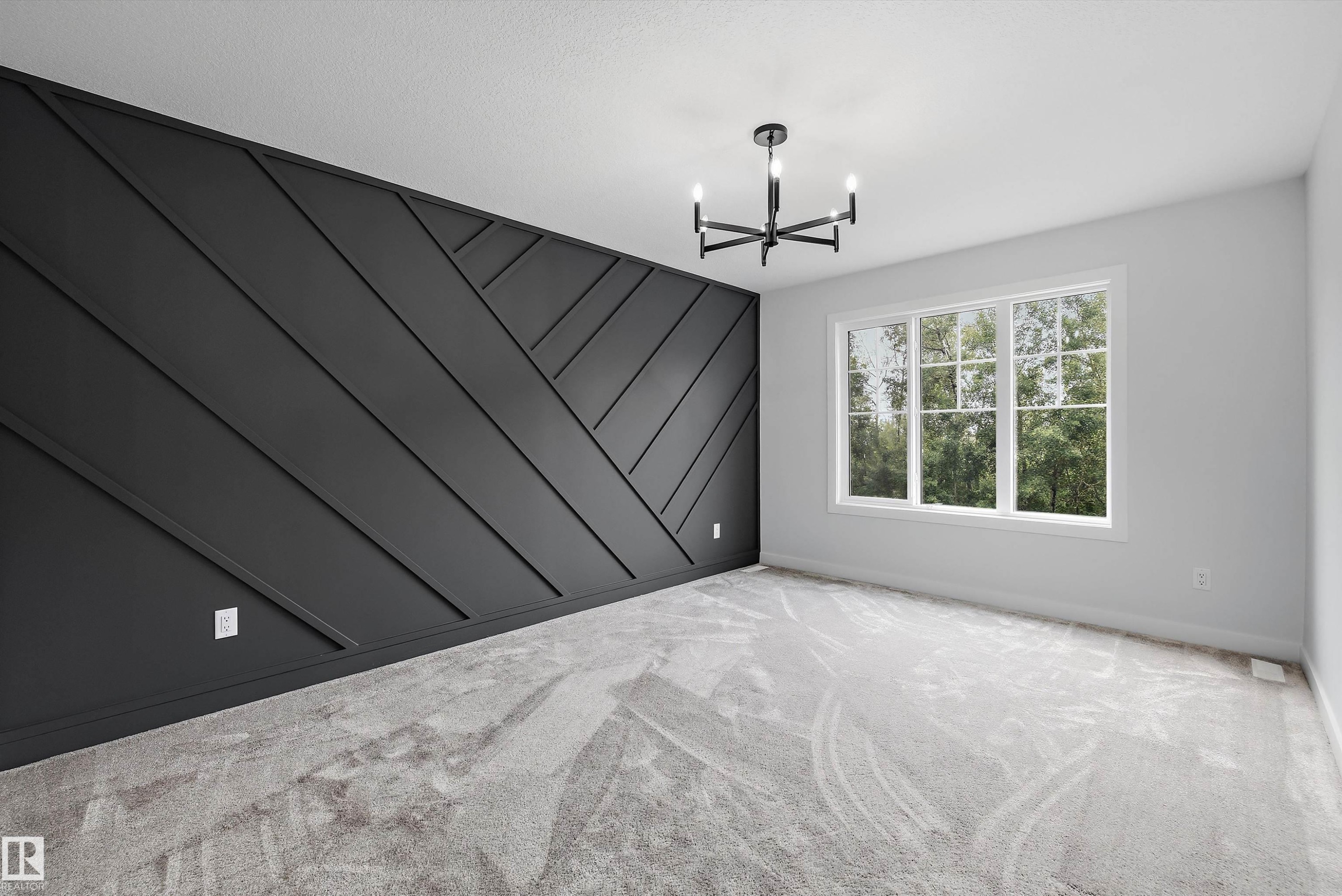 Accent wall featuring geometric paneling, contemporary chandelier, large window with grid pattern, light gray carpeting, and neutral wall paint - 919 Elderberry Landing Nw, Edmonton, AB - Indoor Photo Showing Other Room