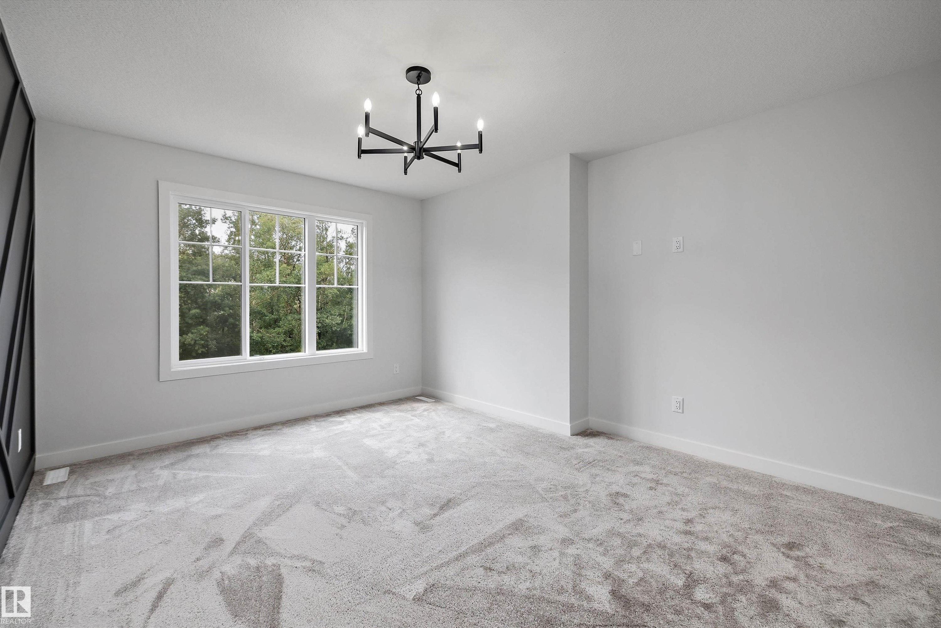 Spacious room featuring a large multi-pane window, contemporary chandelier, light gray carpeting, and white baseboards - 919 Elderberry Landing Nw, Edmonton, AB - Indoor Photo Showing Other Room