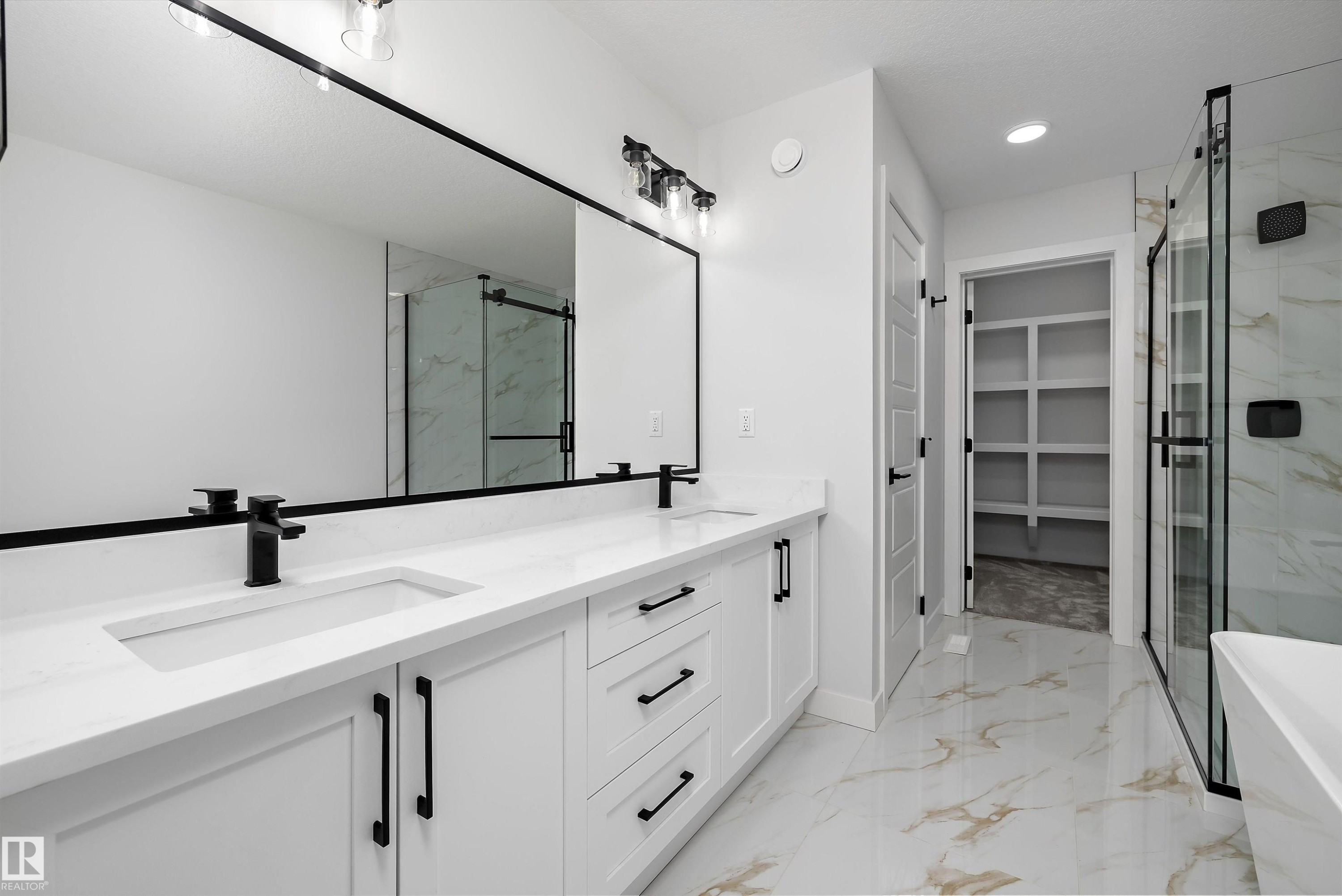 Dual vanity with white cabinetry and matte black hardware, stone-finish countertops, and under-mount sinks - 919 Elderberry Landing Nw, Edmonton, AB - Indoor Photo Showing Bathroom