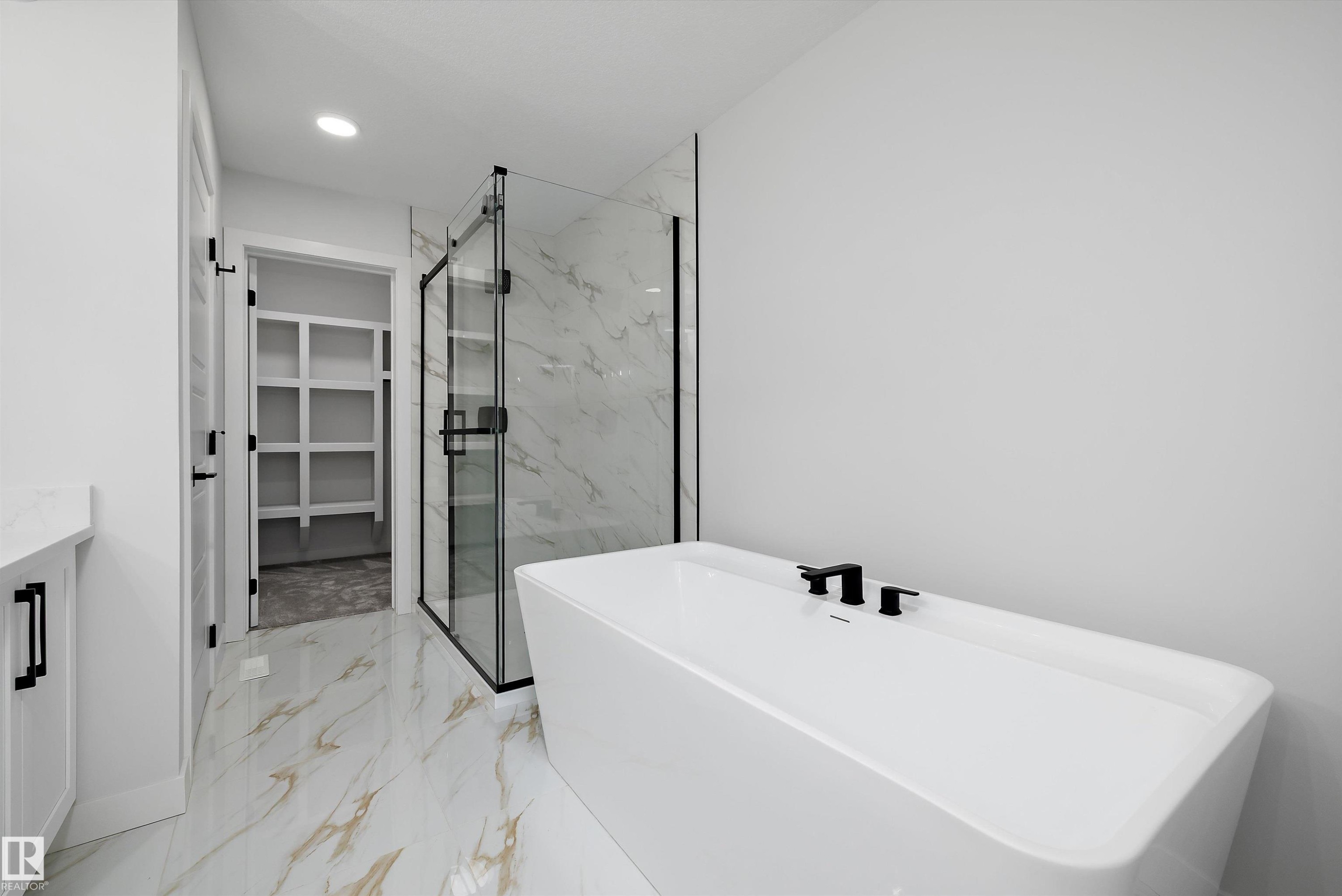 Freestanding soaking tub featuring matte black fixtures, set against a frameless glass shower enclosure with marble-look tile - 919 Elderberry Landing Nw, Edmonton, AB - Indoor Photo Showing Bathroom