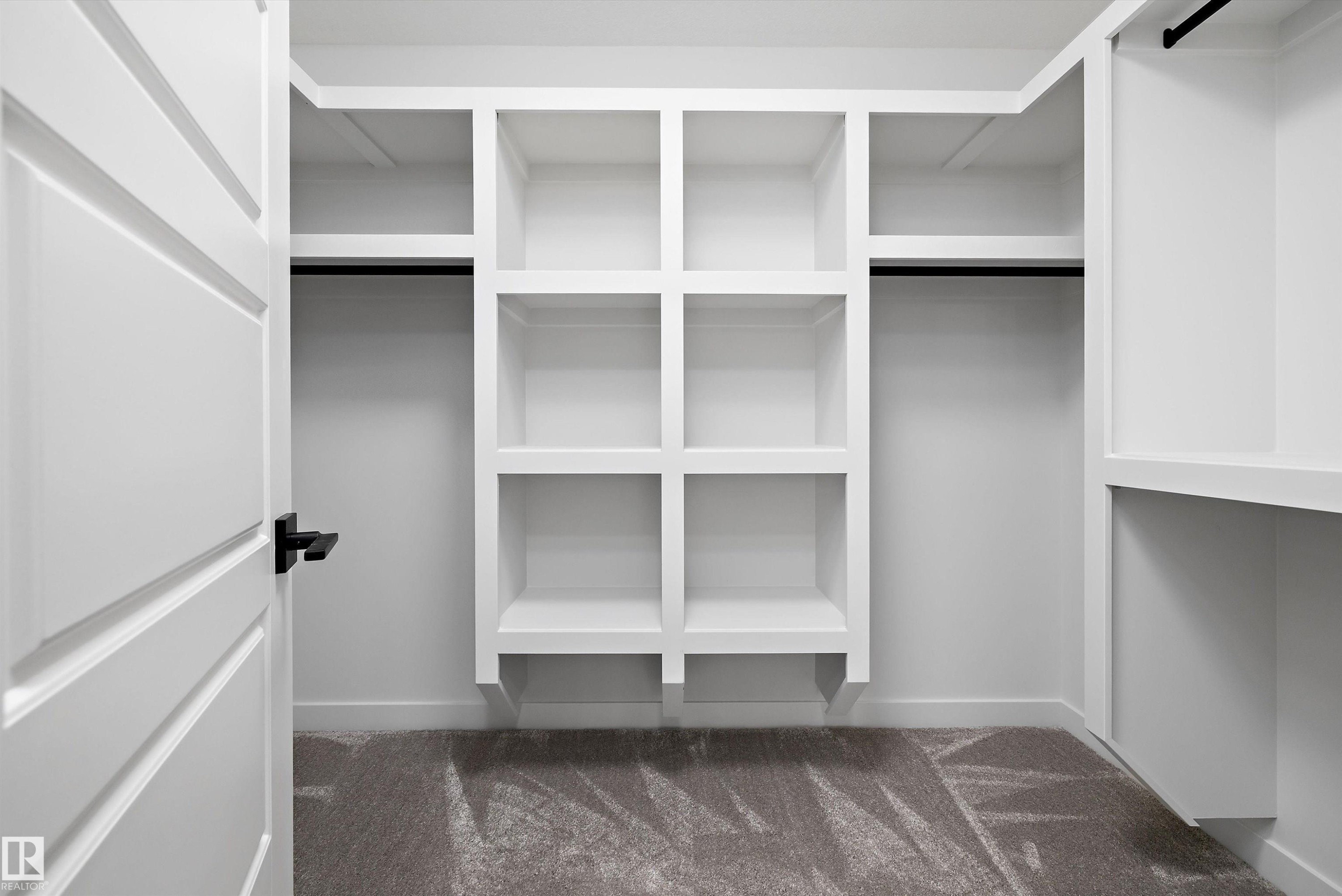 Built-in closet system featuring white shelving units, hanging rods, and patterned carpet flooring - 919 Elderberry Landing Nw, Edmonton, AB - Indoor With Storage