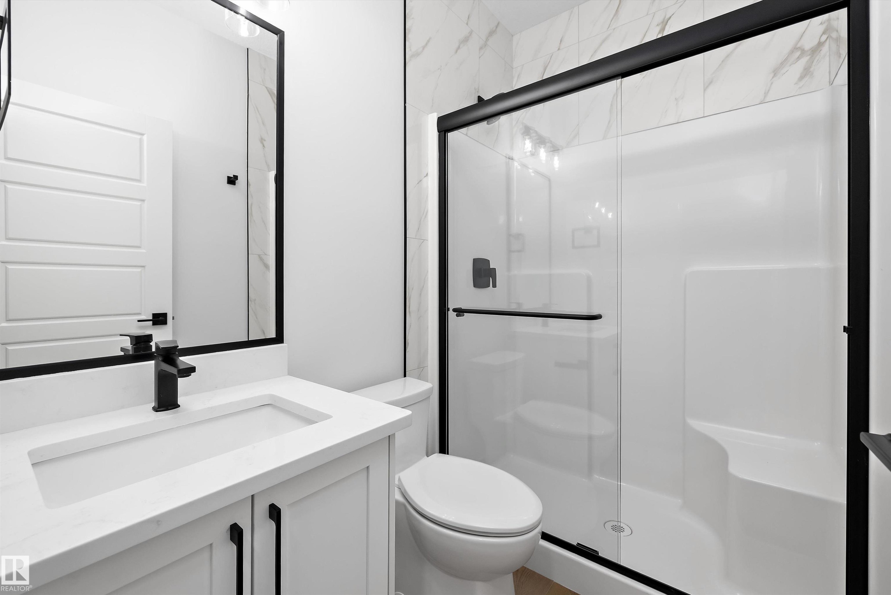 Contemporary bathroom featuring a white vanity with integrated sink, matte black hardware, framed mirror, and a walk-in shower with clear glass enclosure and built-in bench - 919 Elderberry Landing Nw, Edmonton, AB - Indoor Photo Showing Bathroom