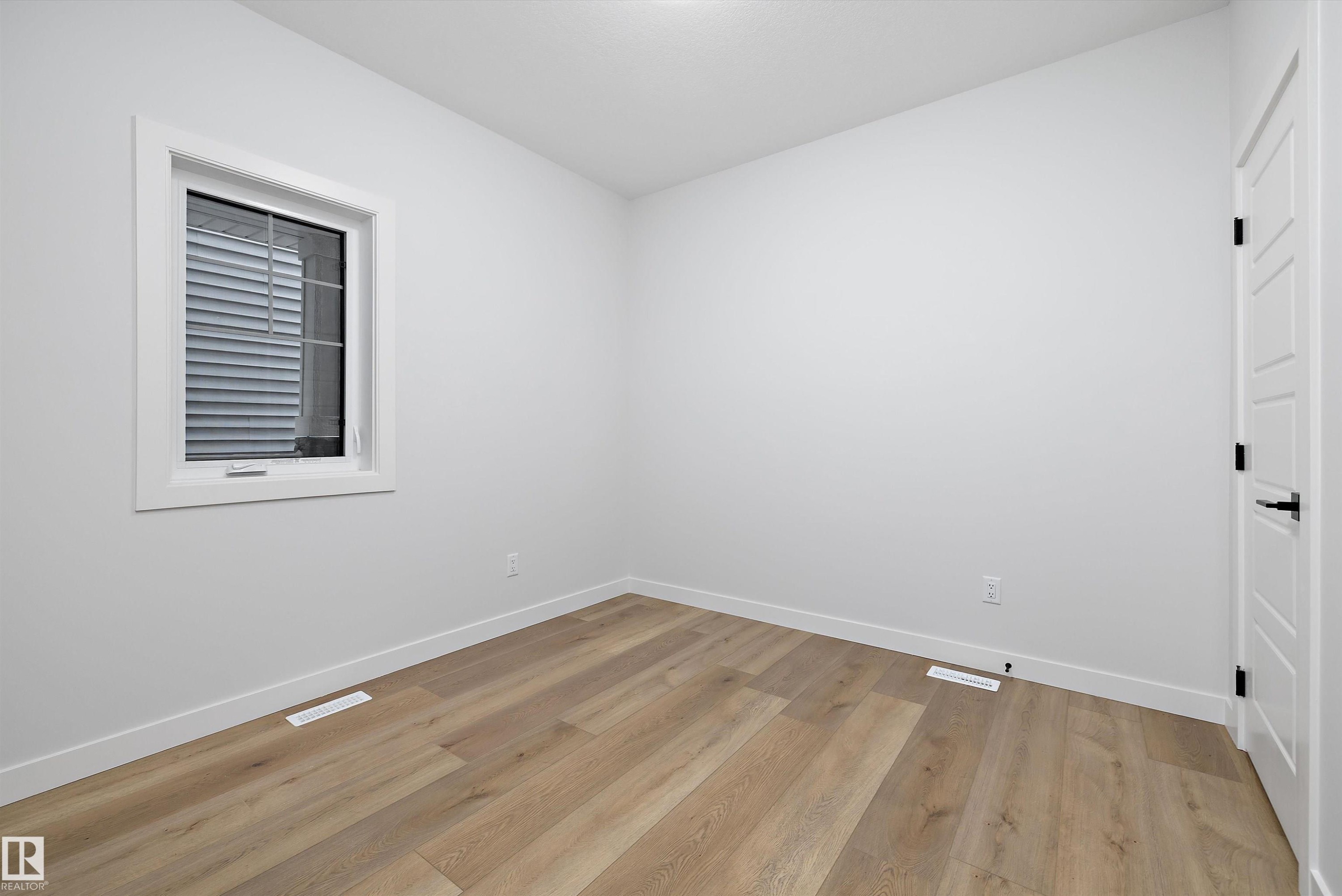 Bright room featuring wood-finish flooring, white baseboards, and a white interior door with black hardware - 919 Elderberry Landing Nw, Edmonton, AB - Indoor Photo Showing Other Room