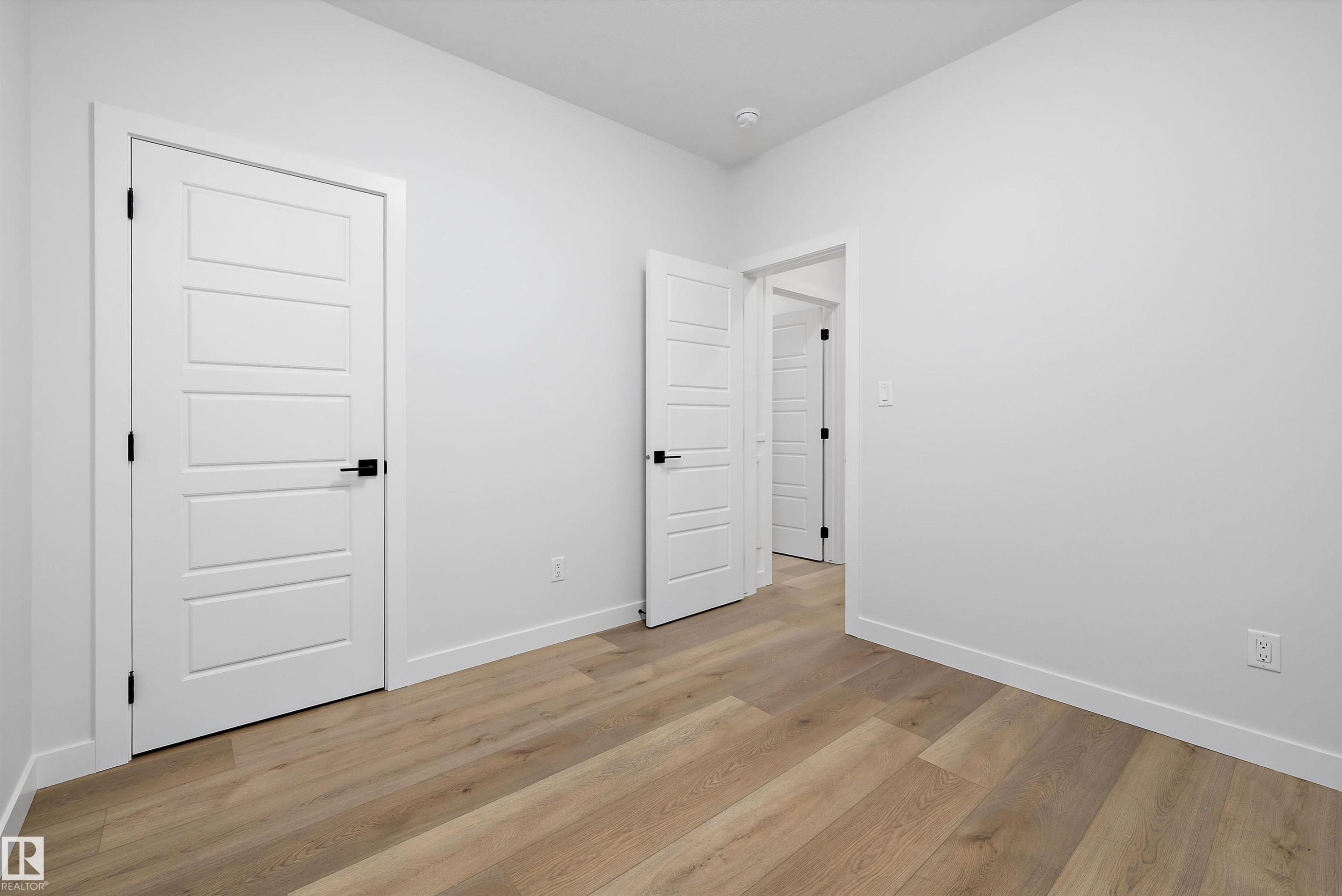 Bright interior room featuring wood-finish flooring, white walls, and contemporary five-panel interior doors with matte black hardware - 919 Elderberry Landing Nw, Edmonton, AB - Indoor Photo Showing Other Room