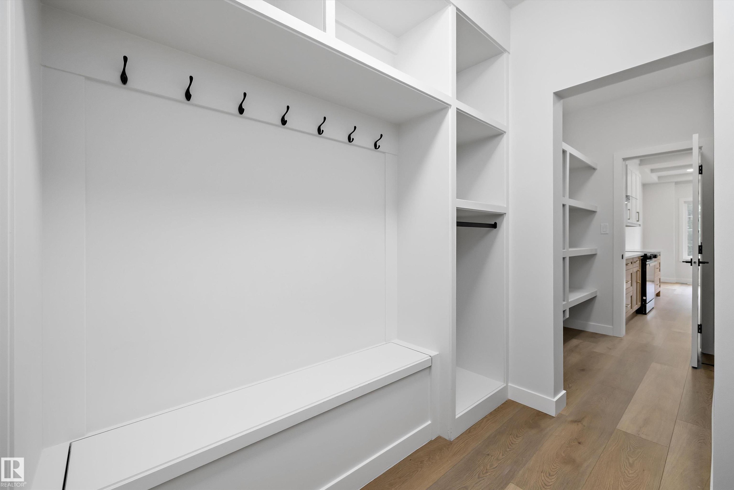 Custom built-in entryway storage featuring a bench seat with lower cabinetry, six wall-mounted coat hooks, and open shelving units - 919 Elderberry Landing Nw, Edmonton, AB - Indoor With Storage