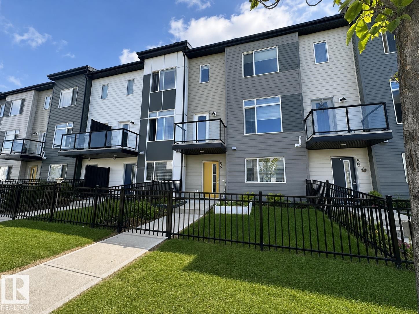 Contemporary townhome exteriors featuring multi-toned siding, black frame windows, and glass panel balconies - #56 804 Welsh Dr Sw, Edmonton, AB - Outdoor With Balcony