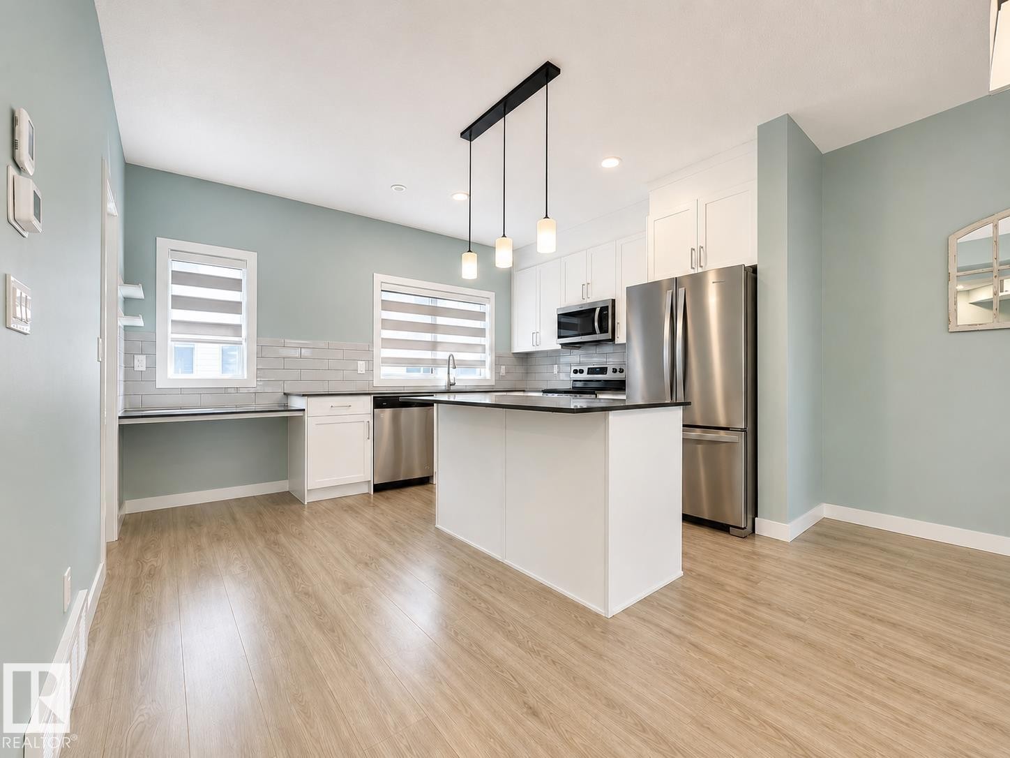 Open-concept kitchen featuring an island, integrated stainless steel appliances, white cabinetry, and wood-finish flooring - #56 804 Welsh Dr Sw, Edmonton, AB - Indoor Photo Showing Kitchen With Stainless Steel Kitchen With Upgraded Kitchen