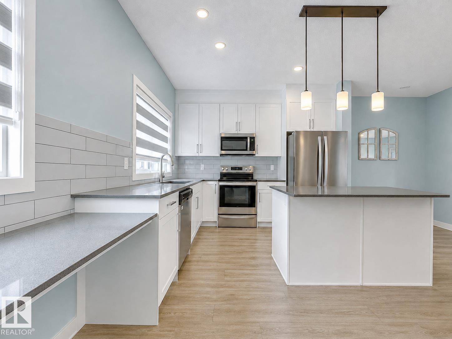 Modern kitchen featuring white cabinetry, stainless steel appliances, a center island with pendant lighting, and wood-finish flooring - #56 804 Welsh Dr Sw, Edmonton, AB - Indoor Photo Showing Kitchen With Stainless Steel Kitchen With Upgraded Kitchen