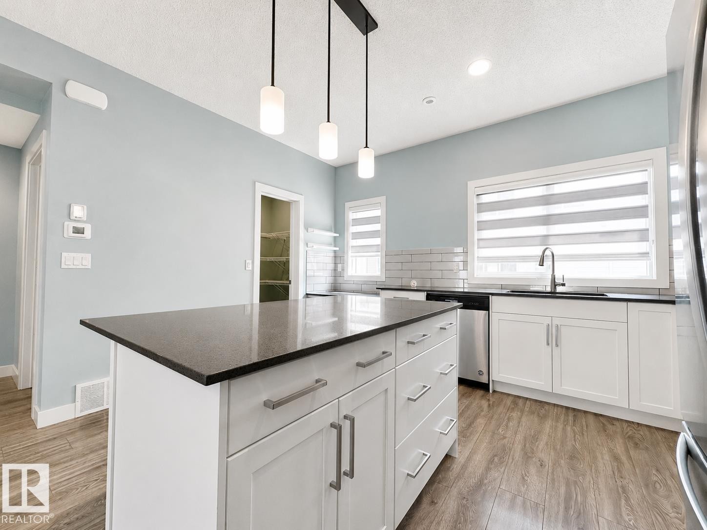 Kitchen featuring a central island with a dark countertop, pendant lighting, white cabinetry, stainless steel appliances, and wood-finish flooring - #56 804 Welsh Dr Sw, Edmonton, AB - Indoor Photo Showing Kitchen With Upgraded Kitchen
