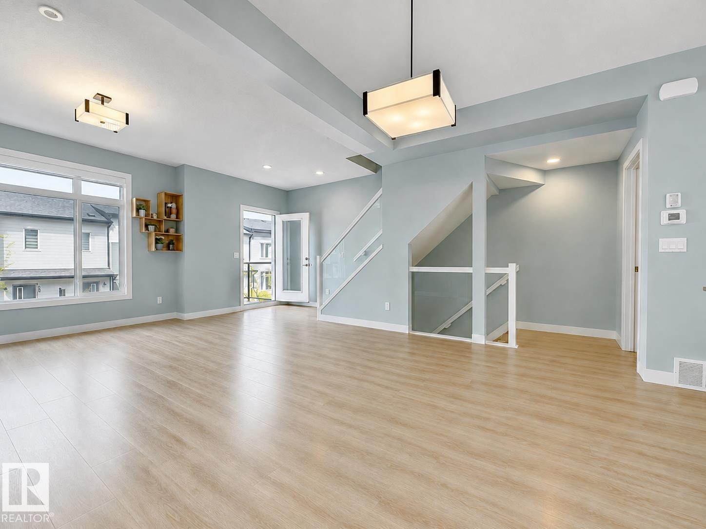 Wood-finish flooring throughout, bright windows, modern lighting fixtures, and a glass-paneled staircase with a white railing - #56 804 Welsh Dr Sw, Edmonton, AB - Indoor