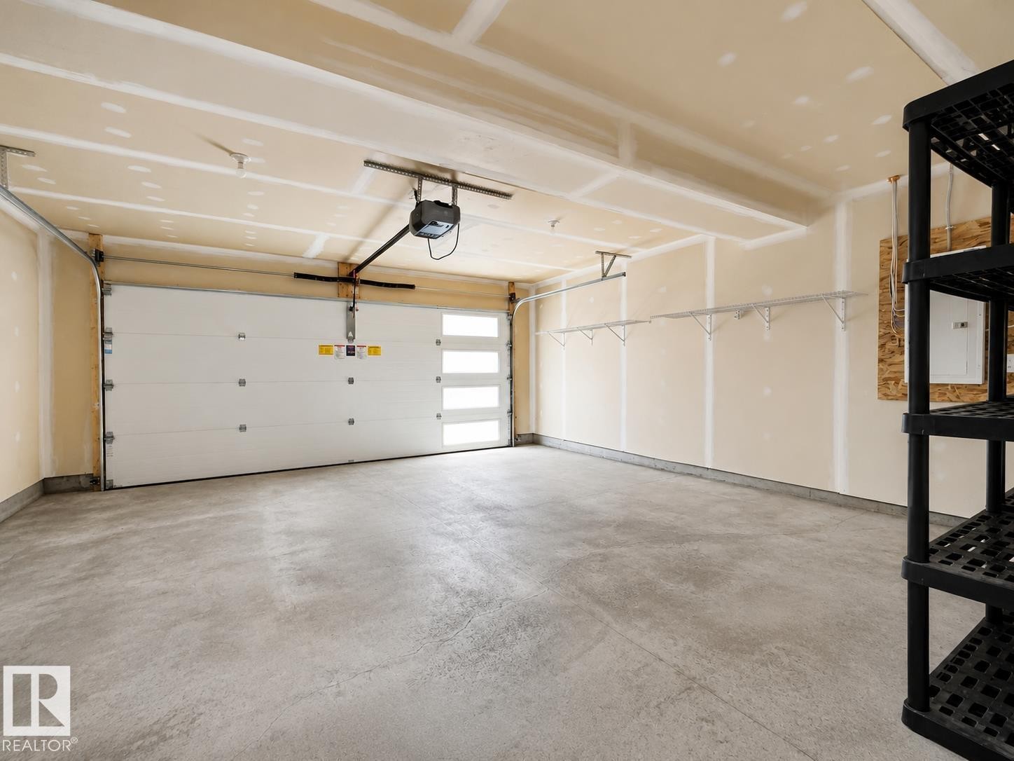 Spacious garage featuring a concrete floor, automatic garage door opener, and integrated wall shelving - #56 804 Welsh Dr Sw, Edmonton, AB - Indoor Photo Showing Garage