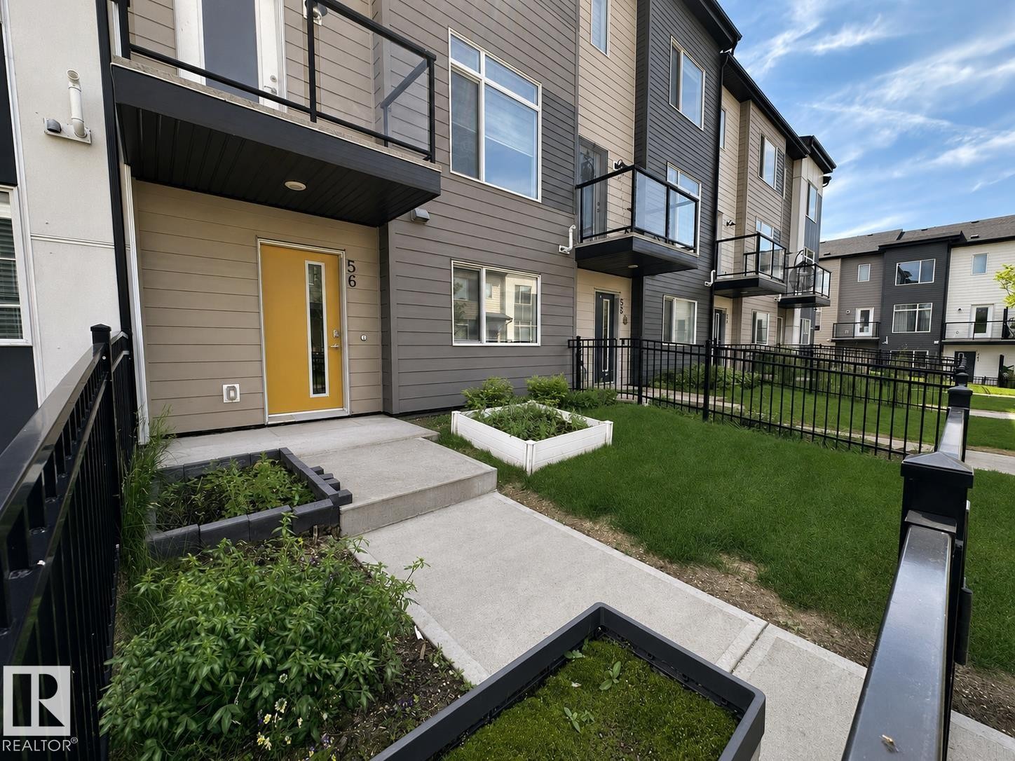 Modern townhome exterior featuring multi-toned siding, a vibrant entry door, and a private balcony with glass railing - #56 804 Welsh Dr Sw, Edmonton, AB - Outdoor With Balcony