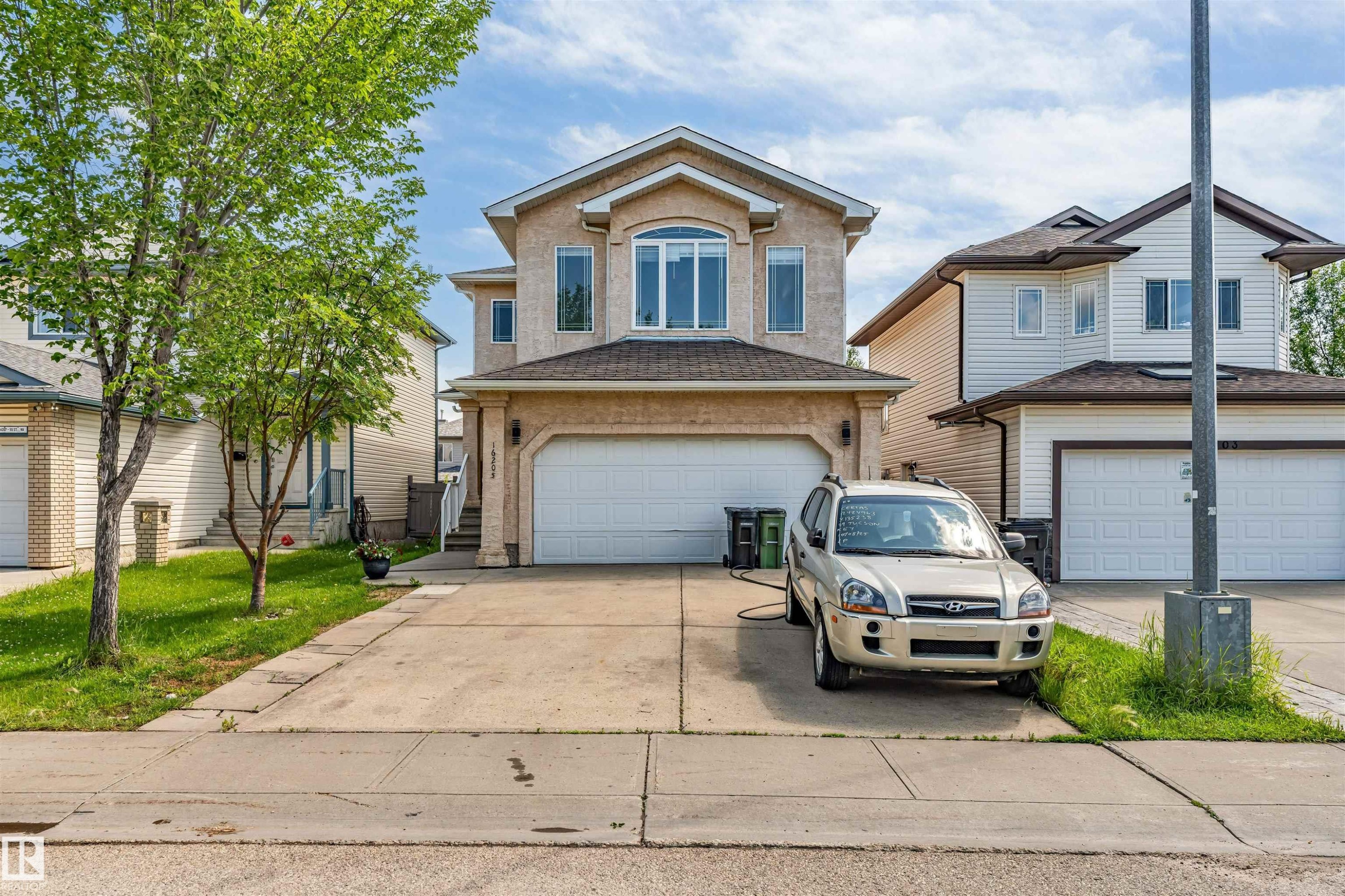 Stucco exterior residence featuring an arched window, multiple vertical windows, attached two-car garage, and concrete driveway - 16205 55 Street Nw, Edmonton, AB - Outdoor With Facade
