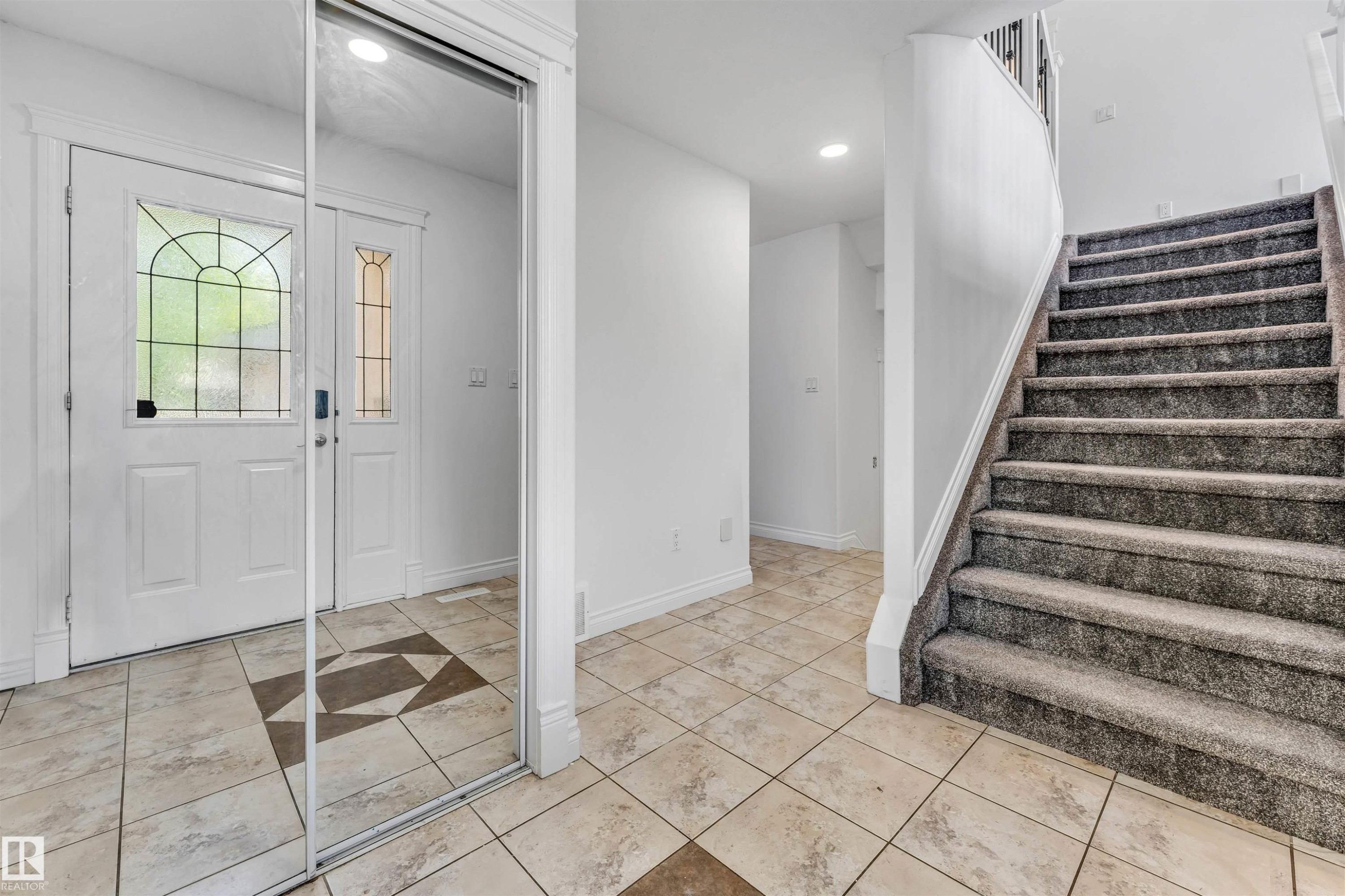 Entry foyer with tile flooring featuring a decorative inlay pattern, a white entry door with leaded glass, and a mirrored closet - 16205 55 Street Nw, Edmonton, AB - Indoor Photo Showing Other Room