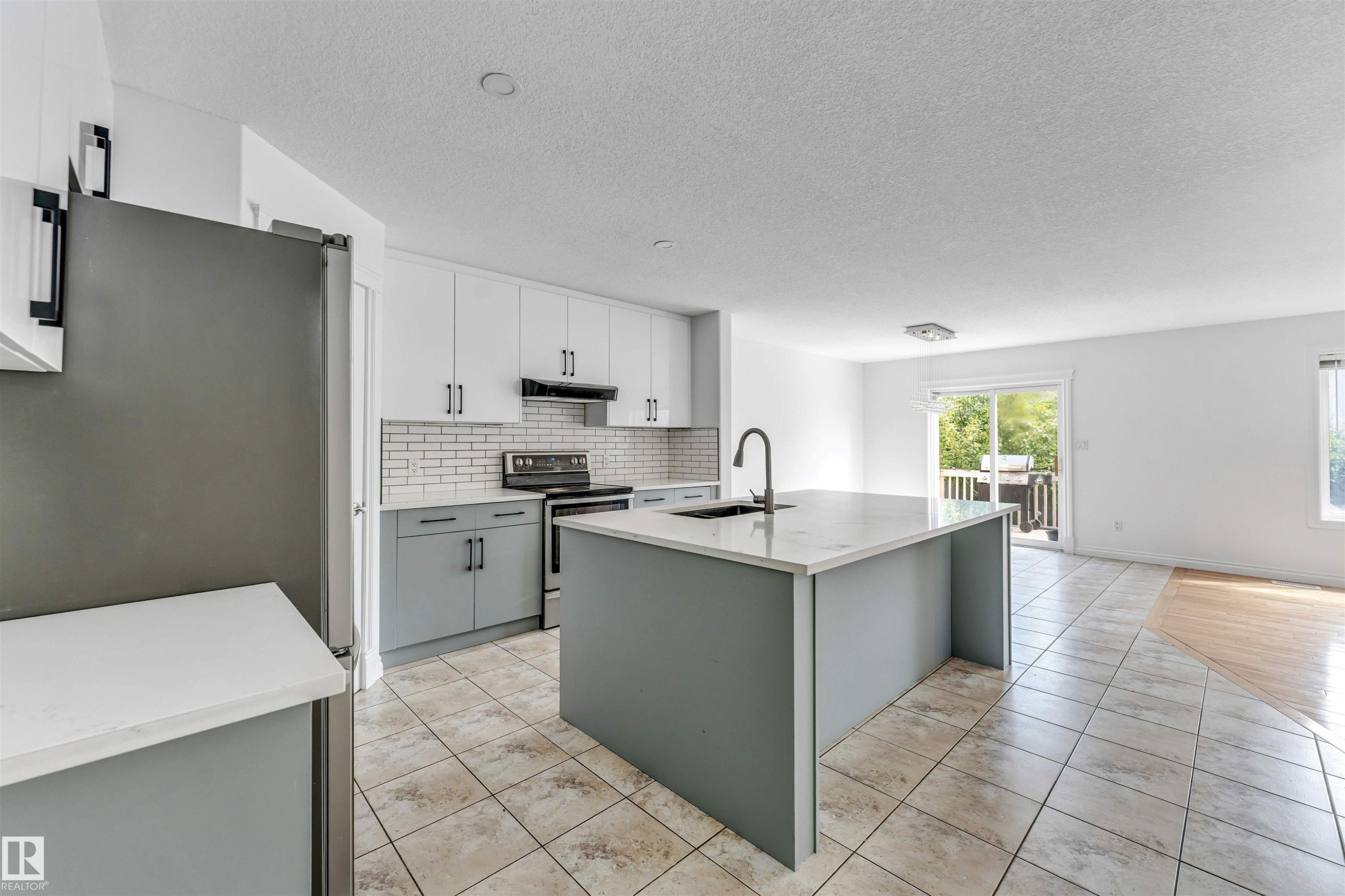 Modern kitchen featuring a large central island with a sink and gooseneck faucet, two-tone cabinetry, subway tile backsplash, and stainless steel appliances - 16205 55 Street Nw, Edmonton, AB - Indoor Photo Showing Kitchen With Upgraded Kitchen