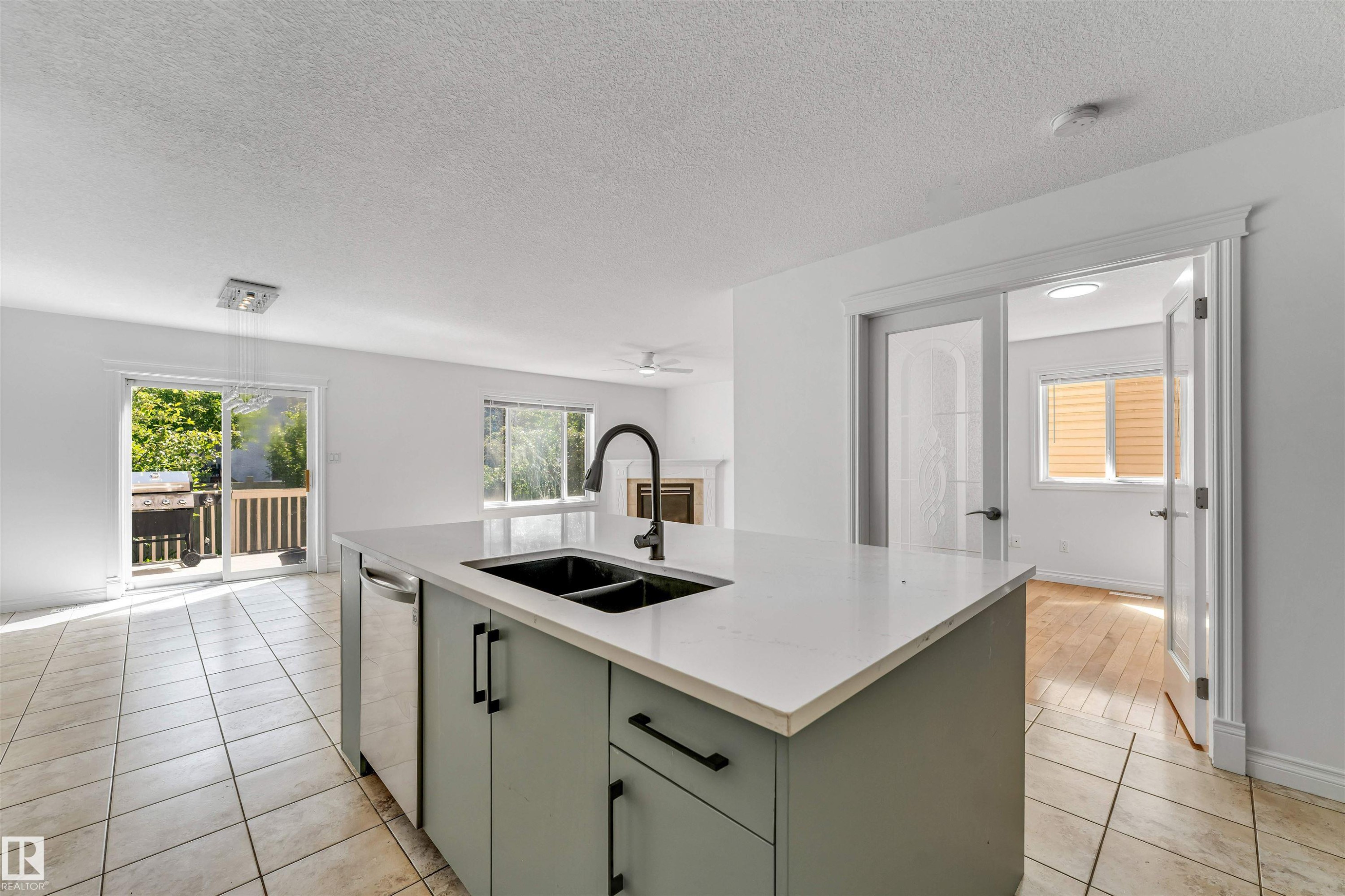 Central kitchen island with a double basin sink and matte black faucet, featuring an integrated dishwasher and light green cabinetry with matte black hardware - 16205 55 Street Nw, Edmonton, AB - Indoor Photo Showing Kitchen With Double Sink