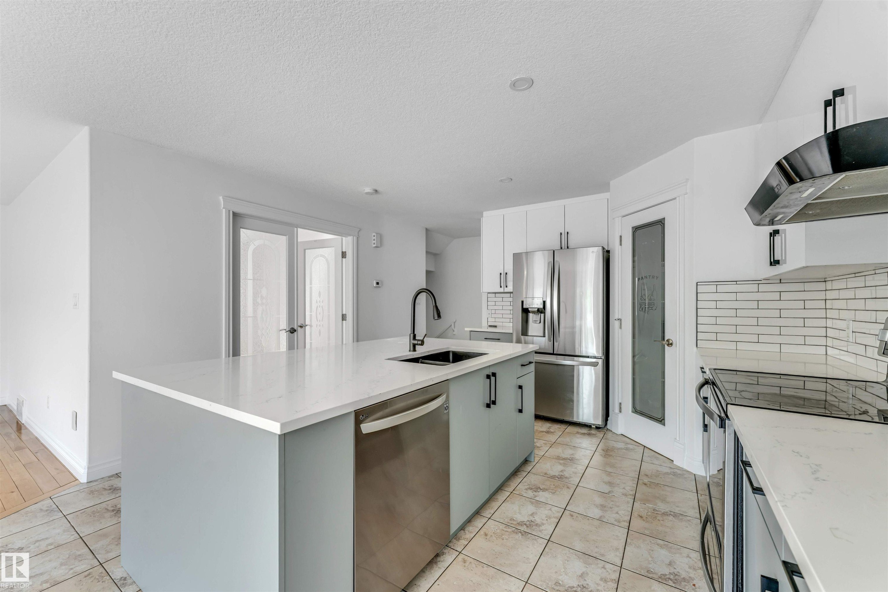 Kitchen featuring a large central island with light-toned countertop, stainless steel appliances, white cabinetry, and tile flooring - 16205 55 Street Nw, Edmonton, AB - Indoor Photo Showing Kitchen With Upgraded Kitchen