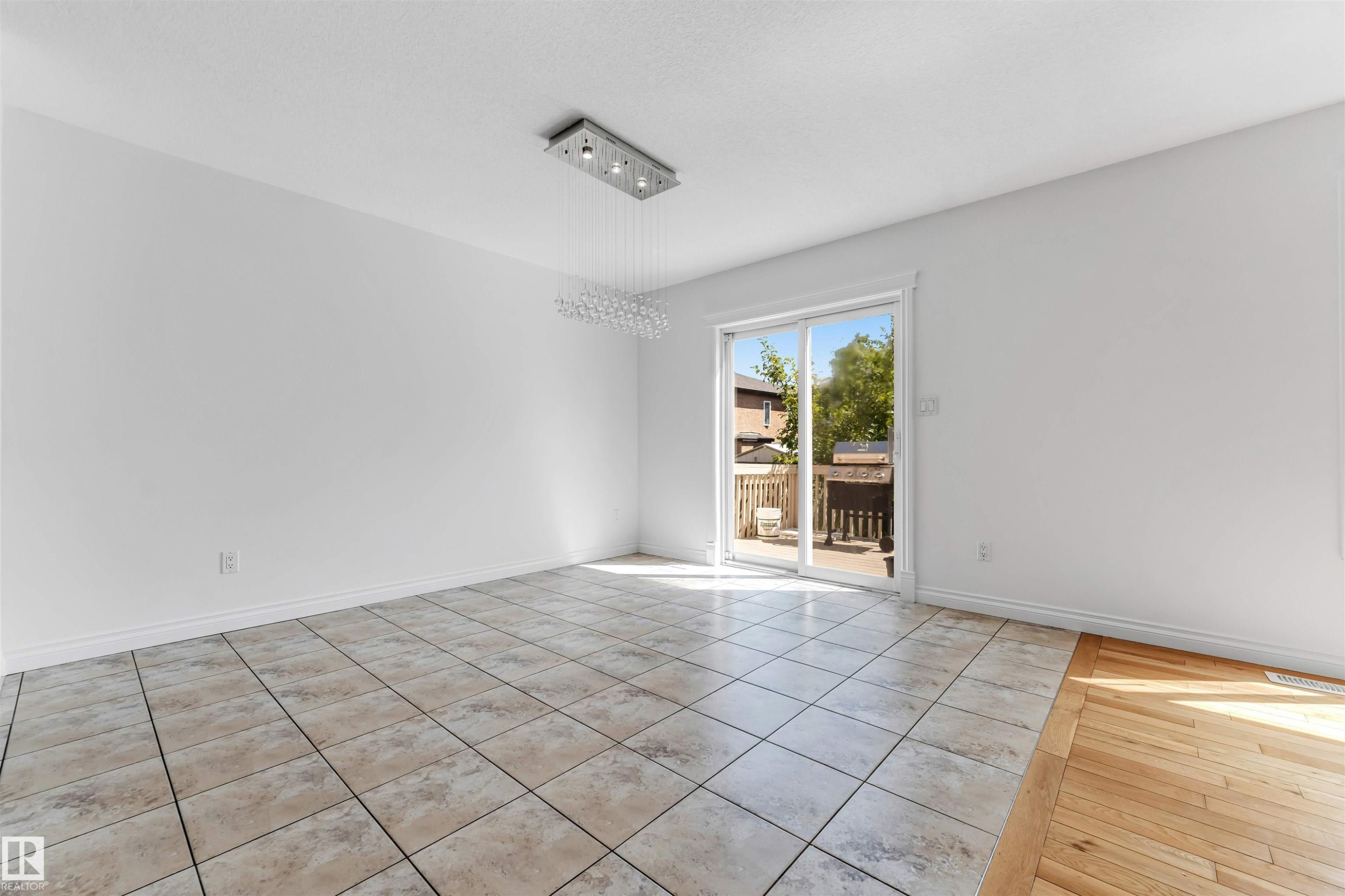 Spacious room with large format tile flooring and a decorative rectangular chandelier - 16205 55 Street Nw, Edmonton, AB - Indoor Photo Showing Other Room