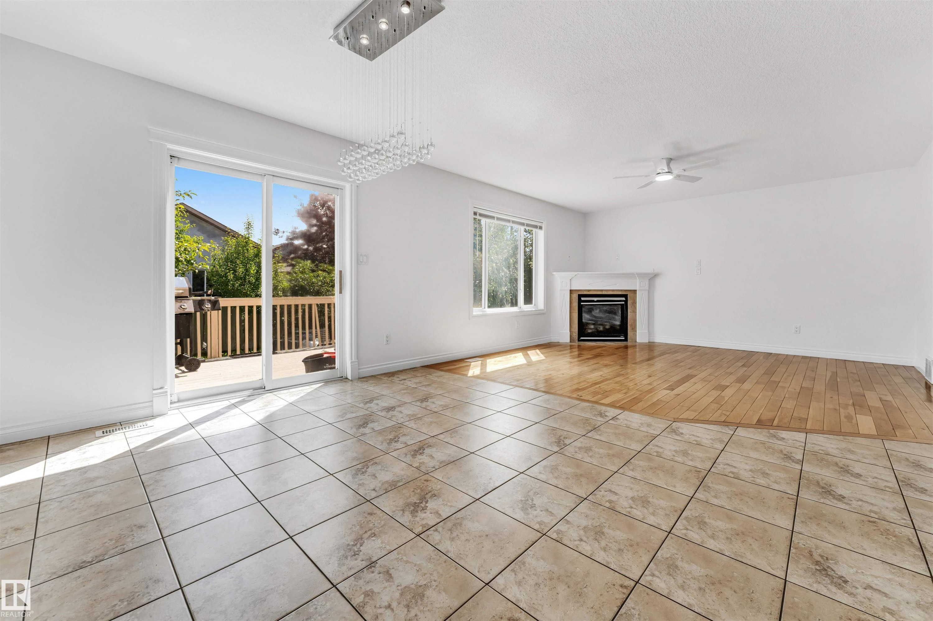 Interior space featuring ceramic tile flooring, hardwood flooring, a white mantel fireplace, a ceiling fan, and a crystal chandelier - 16205 55 Street Nw, Edmonton, AB - Indoor