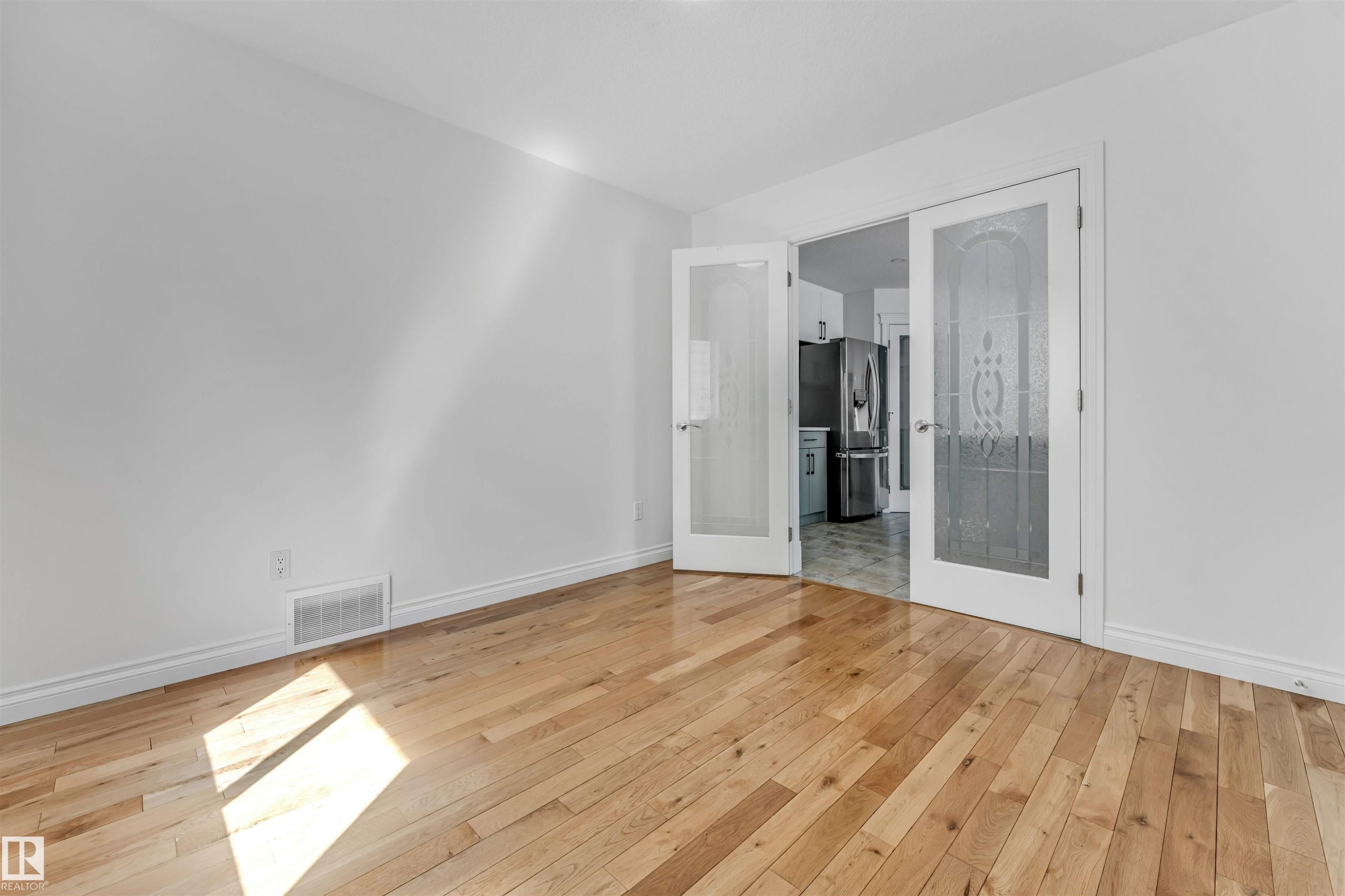 Spacious room featuring wood-finish flooring, white baseboards, and bright white walls - 16205 55 Street Nw, Edmonton, AB - Indoor Photo Showing Other Room