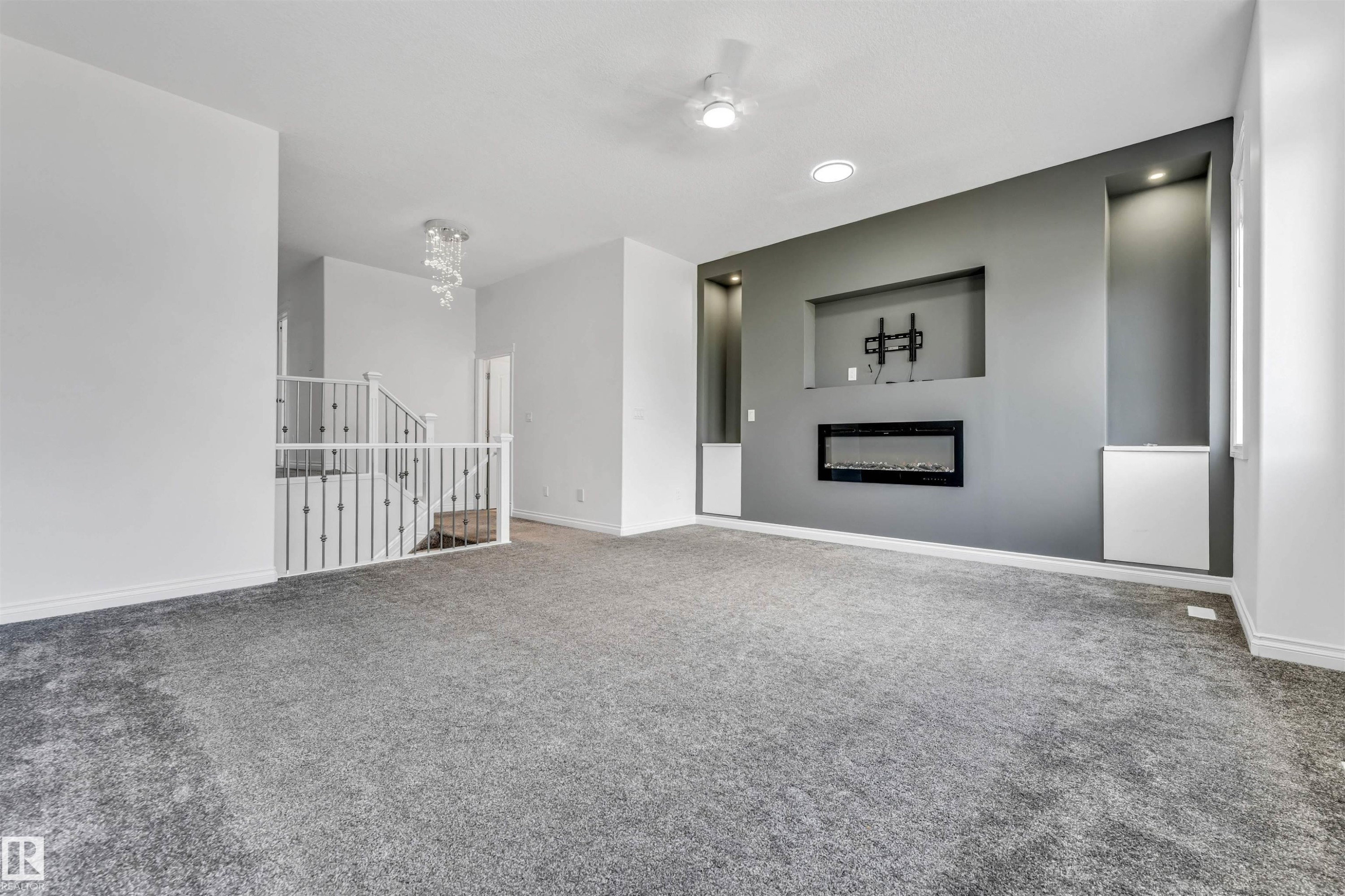 Spacious room featuring gray carpeting, an accent wall with a built-in electric fireplace, recessed lighting, and wall niches with integrated illumination - 16205 55 Street Nw, Edmonton, AB - Indoor With Fireplace