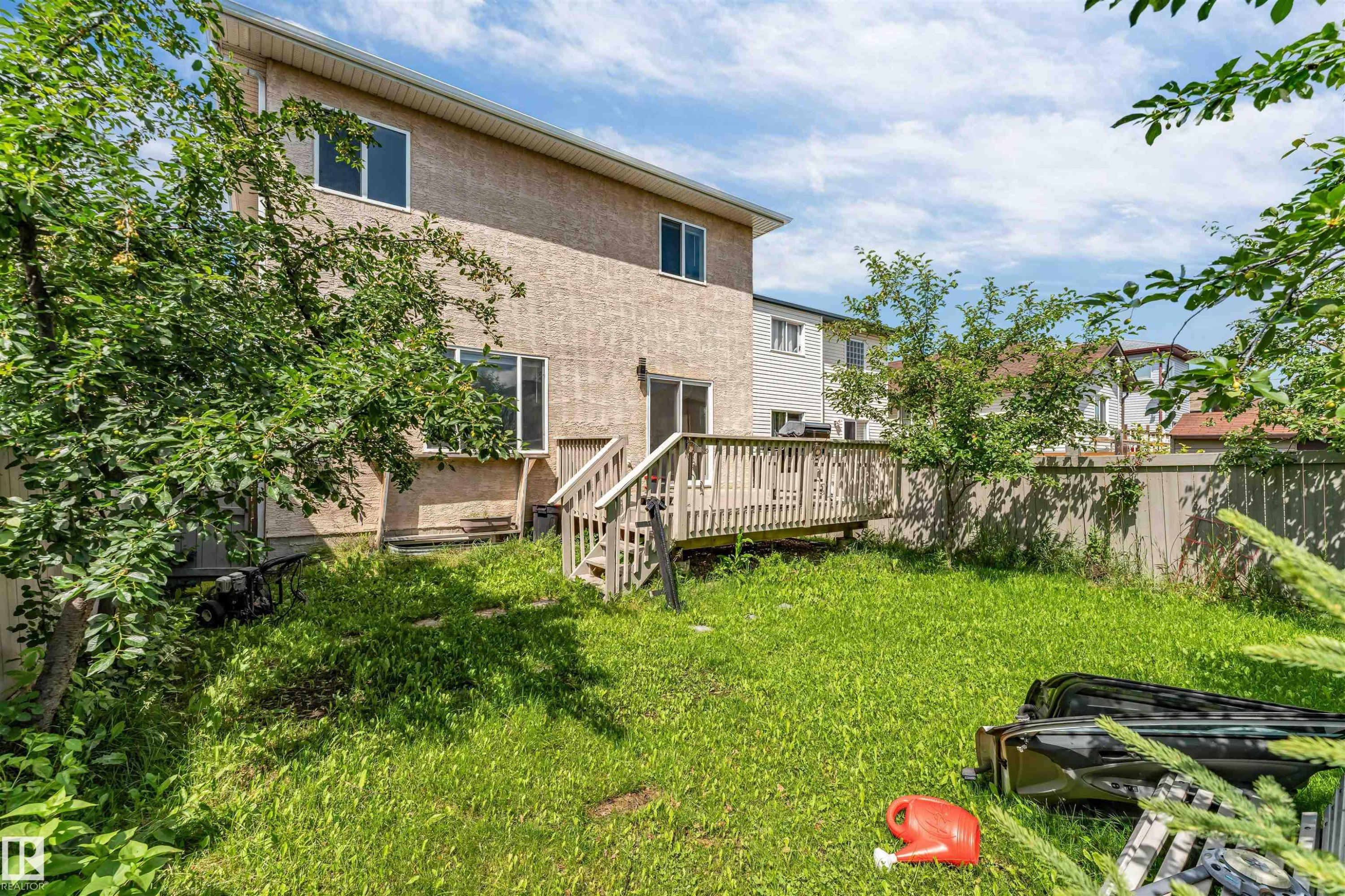 Rear exterior featuring a wood deck with stairs, stucco siding, and multiple windows - 16205 55 Street Nw, Edmonton, AB - Outdoor With Deck Patio Veranda