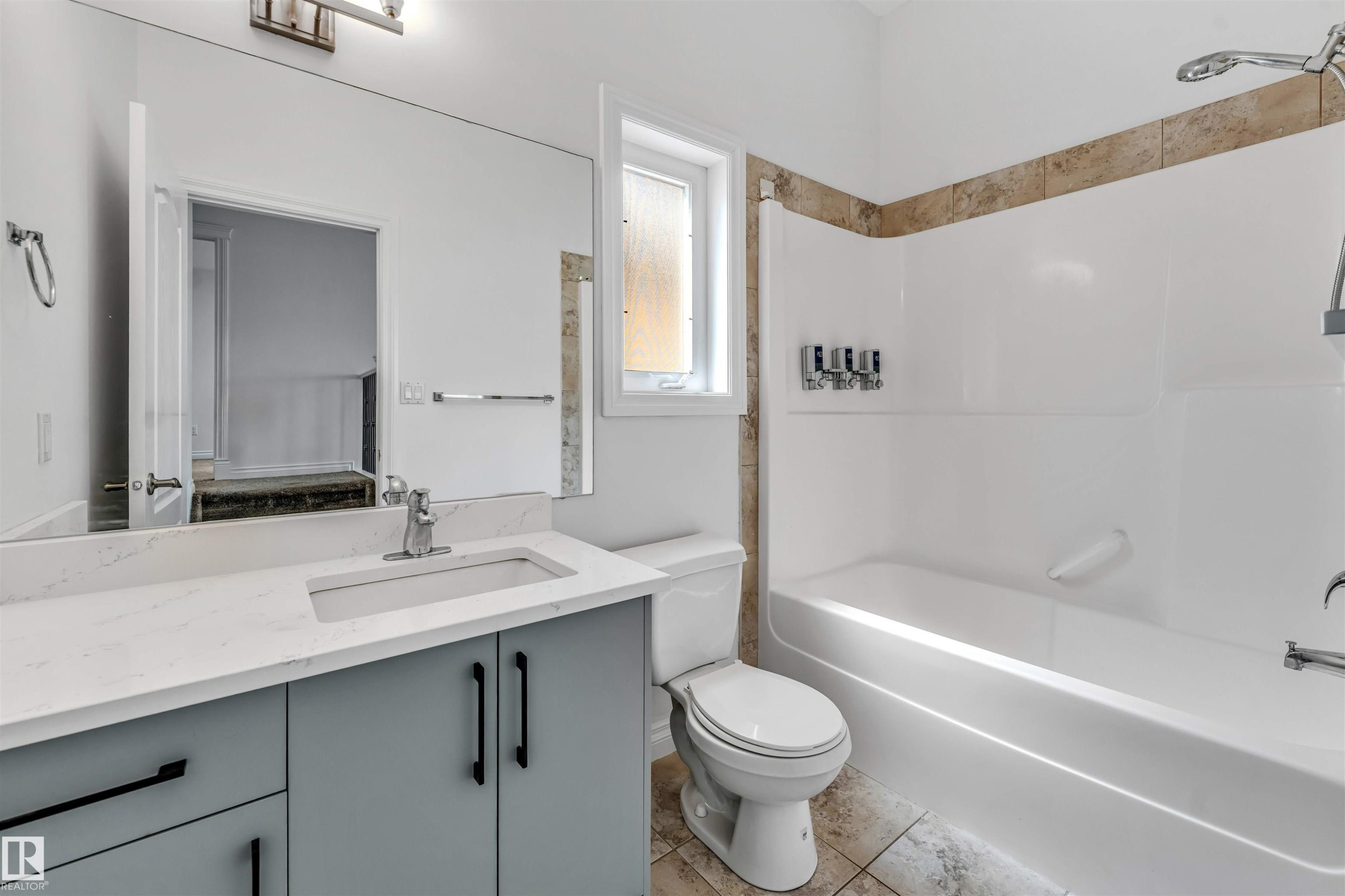Bathroom featuring a spacious vanity with a white countertop and gray cabinetry, an integrated sink with a chrome faucet, a large wall-mounted mirror, and a tub/shower combination with a tiled surround - 16205 55 Street Nw, Edmonton, AB - Indoor Photo Showing Bathroom