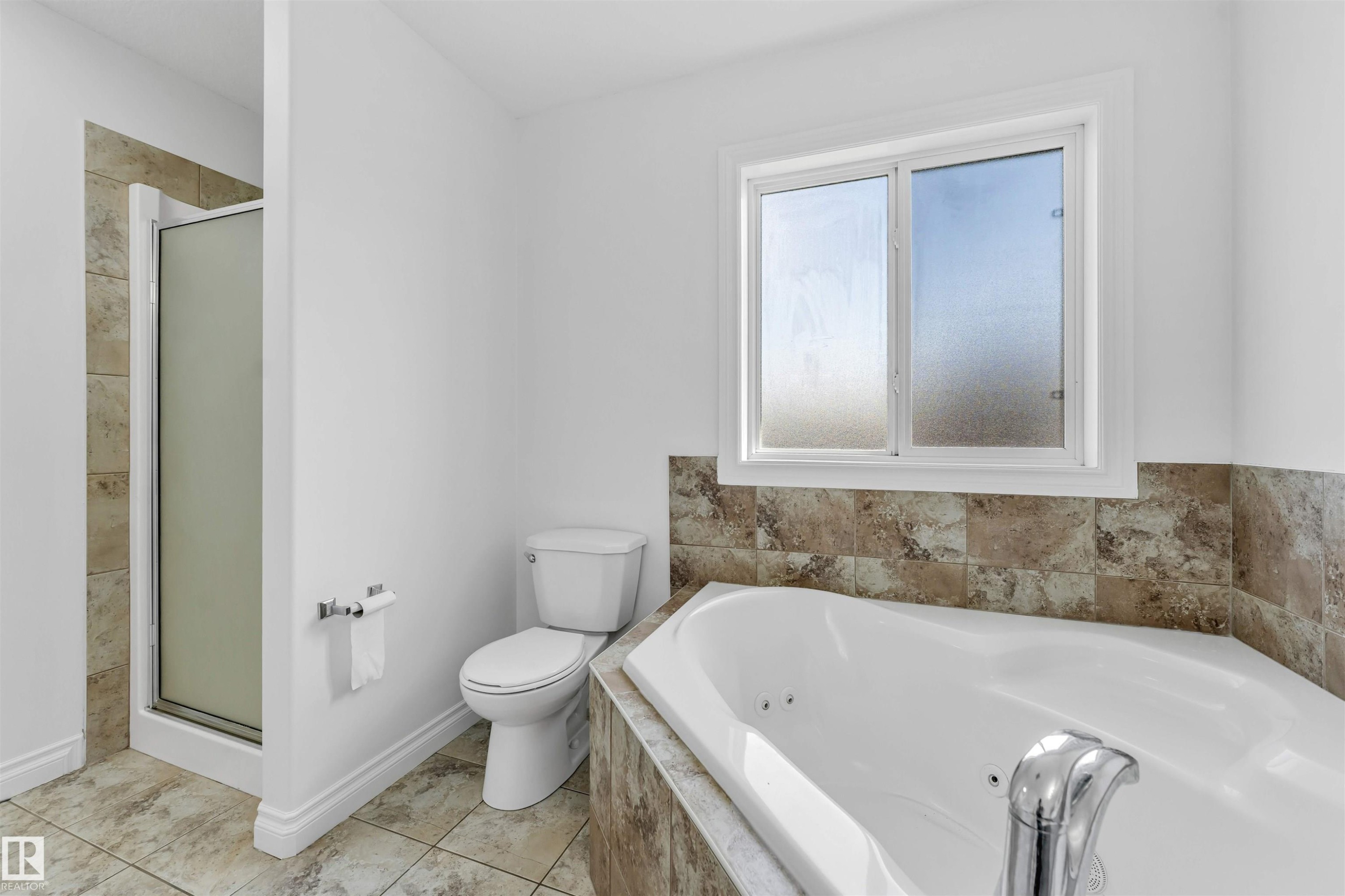 Bathroom featuring a built-in jetted tub with tile surround, a separate shower enclosure with a frosted glass door, and a white toilet - 16205 55 Street Nw, Edmonton, AB - Indoor Photo Showing Bathroom
