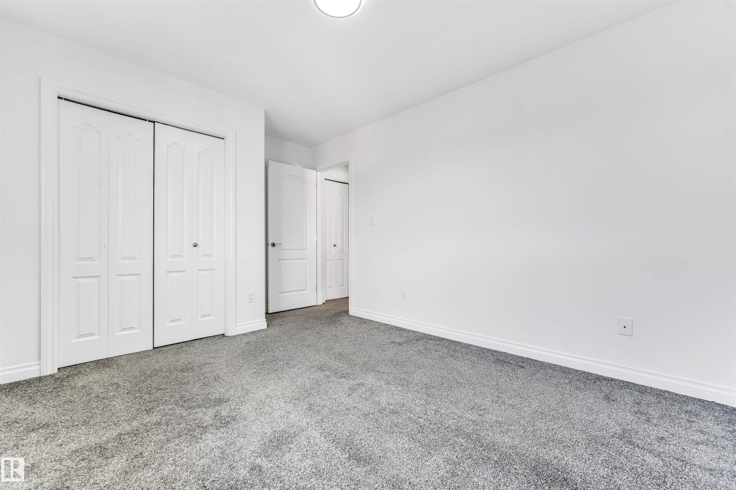 Neutral white wall finishes, crisp white trim, and bi-fold closet doors - 16205 55 Street Nw, Edmonton, AB - Indoor Photo Showing Other Room