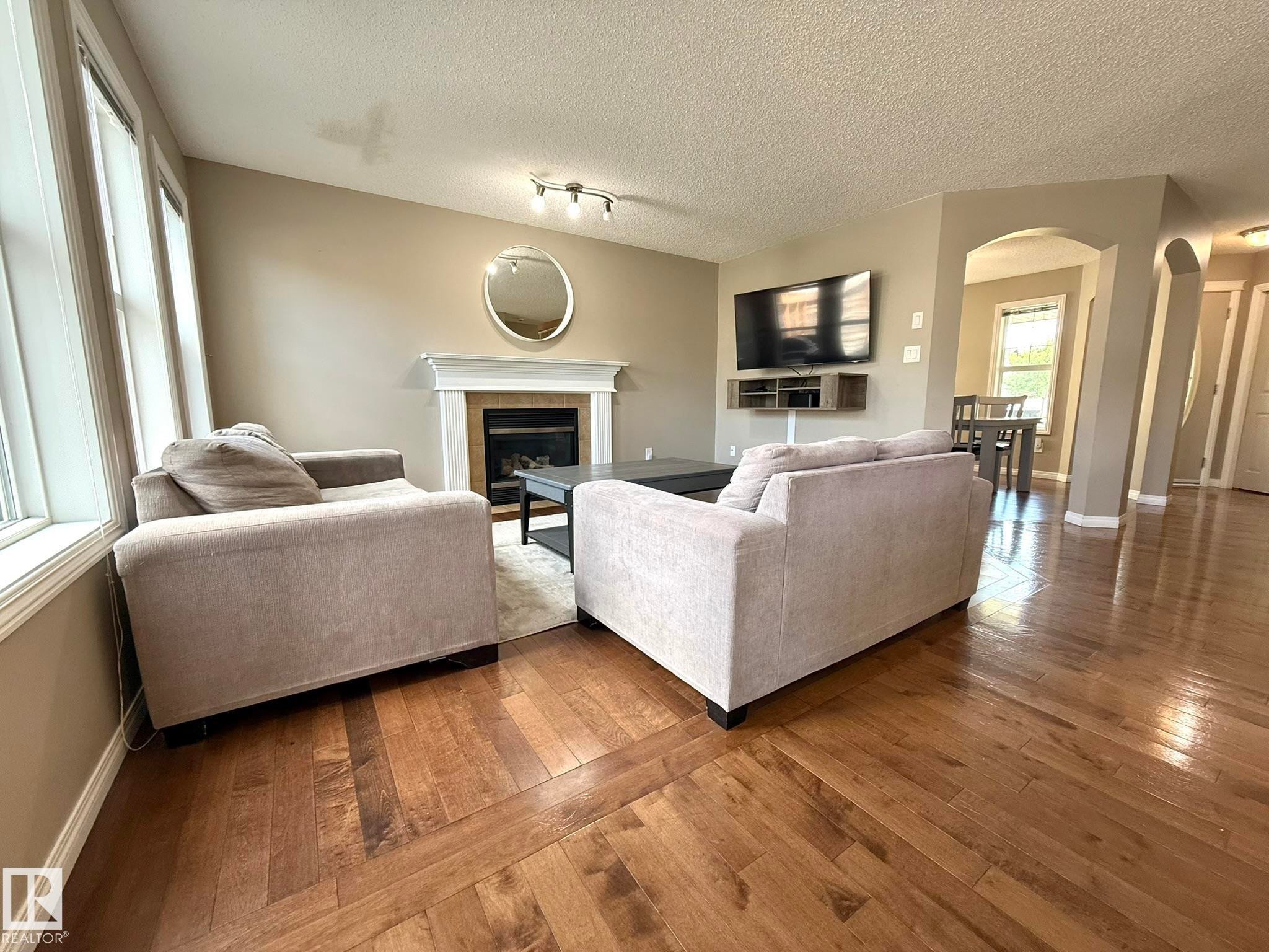 Living area featuring wood-finish flooring, a fireplace with a white mantel, and track lighting - 1820 Robertson Crescent Sw, Edmonton, AB - Indoor Photo Showing Living Room With Fireplace