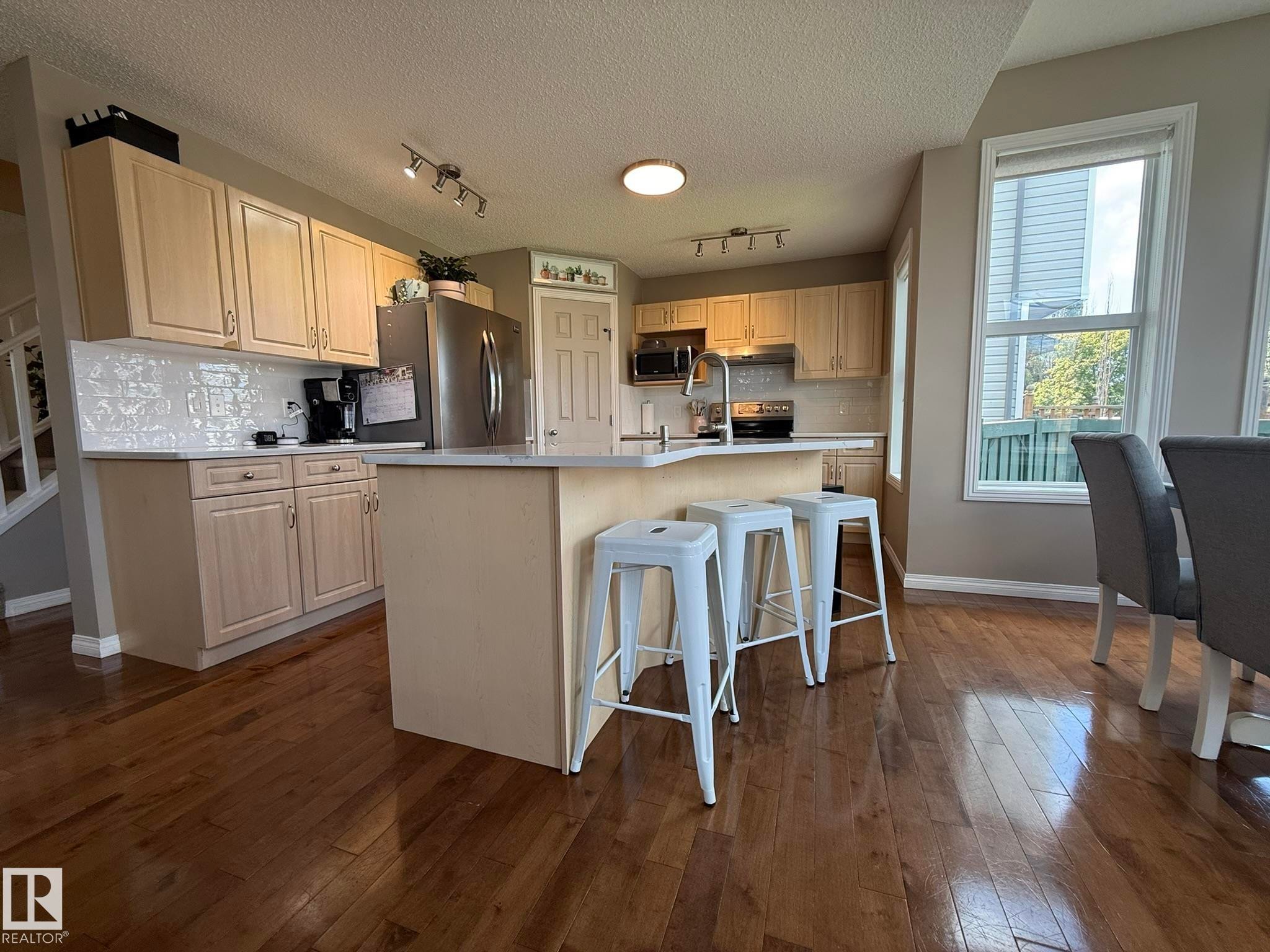 Kitchen featuring light wood-finish cabinetry, a central island with countertop seating, stainless steel appliances, and a tiled backsplash - 1820 Robertson Crescent Sw, Edmonton, AB - Indoor Photo Showing Kitchen