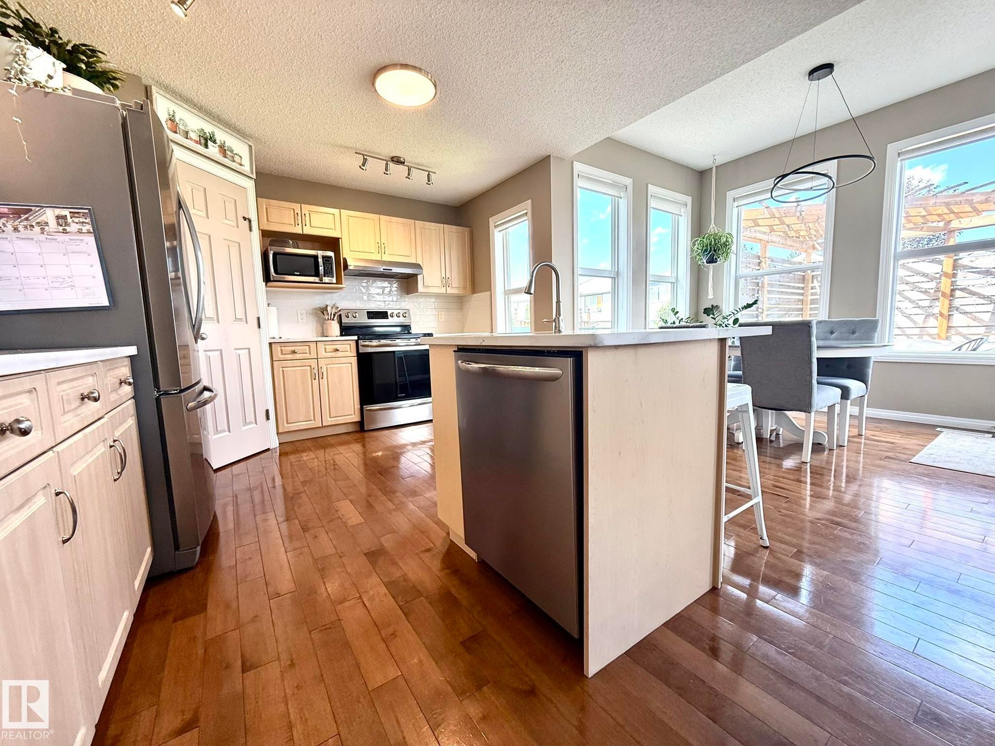 Kitchen featuring wood-finish flooring, light-toned cabinetry, stainless steel appliances, and an island with an integrated sink - 1820 Robertson Crescent Sw, Edmonton, AB - Indoor Photo Showing Kitchen