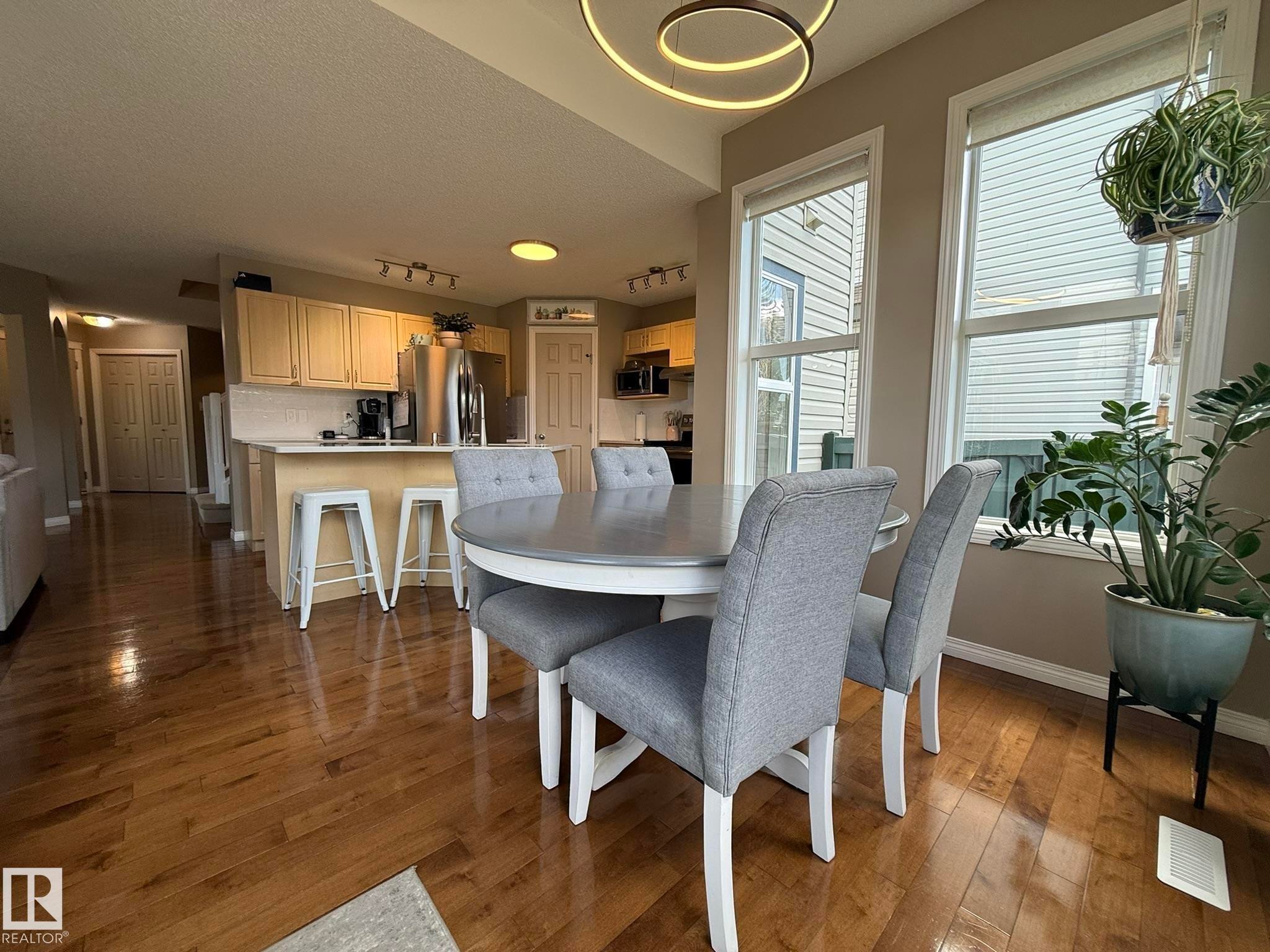 Integrated kitchen and dining area featuring wood-finish flooring, a contemporary circular pendant light, and two large windows - 1820 Robertson Crescent Sw, Edmonton, AB - Indoor Photo Showing Dining Room