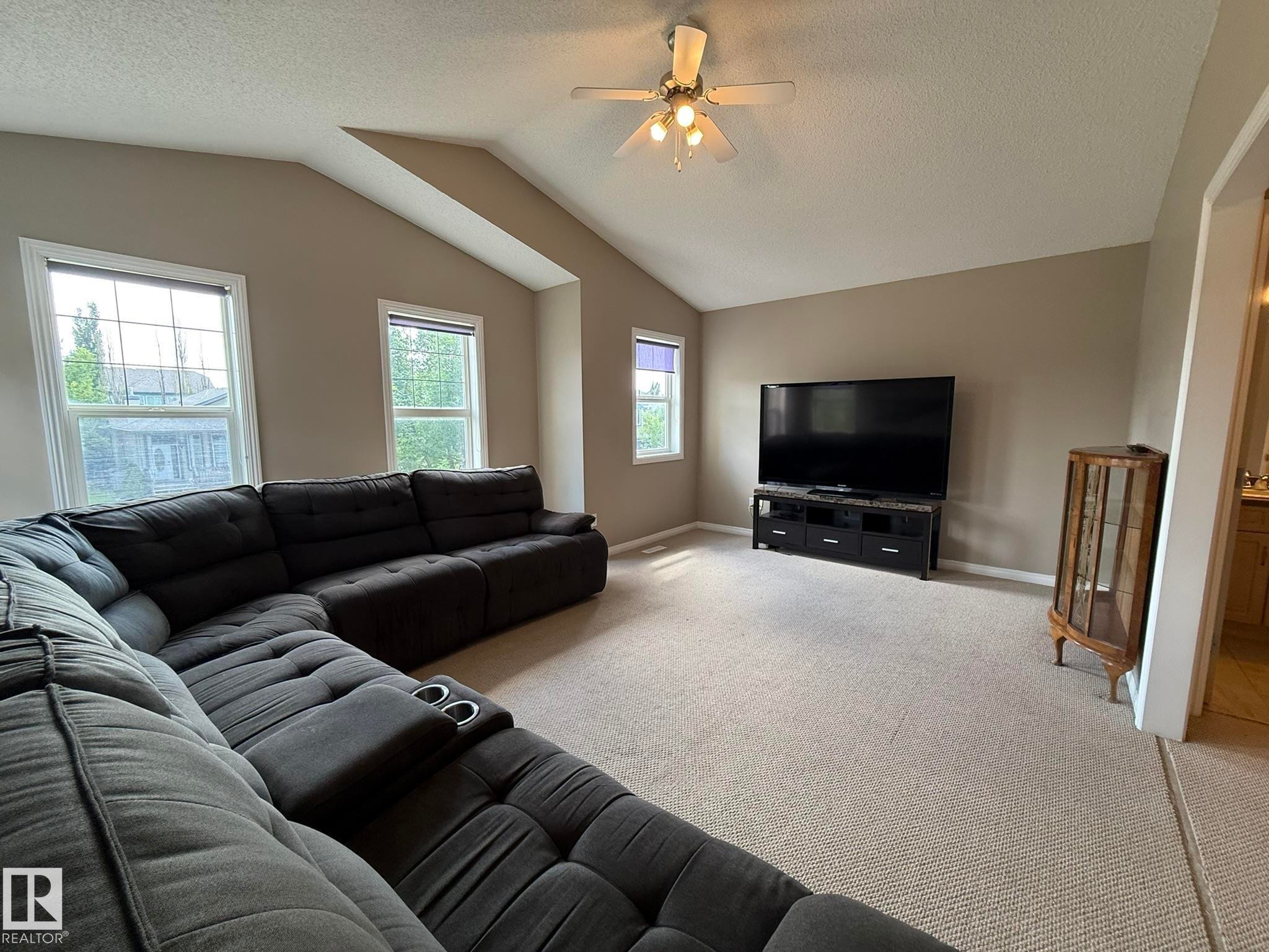 Spacious living area featuring vaulted ceilings, light-colored carpeting, multiple windows, and a ceiling fan with integrated lighting - 1820 Robertson Crescent Sw, Edmonton, AB - Indoor Photo Showing Living Room