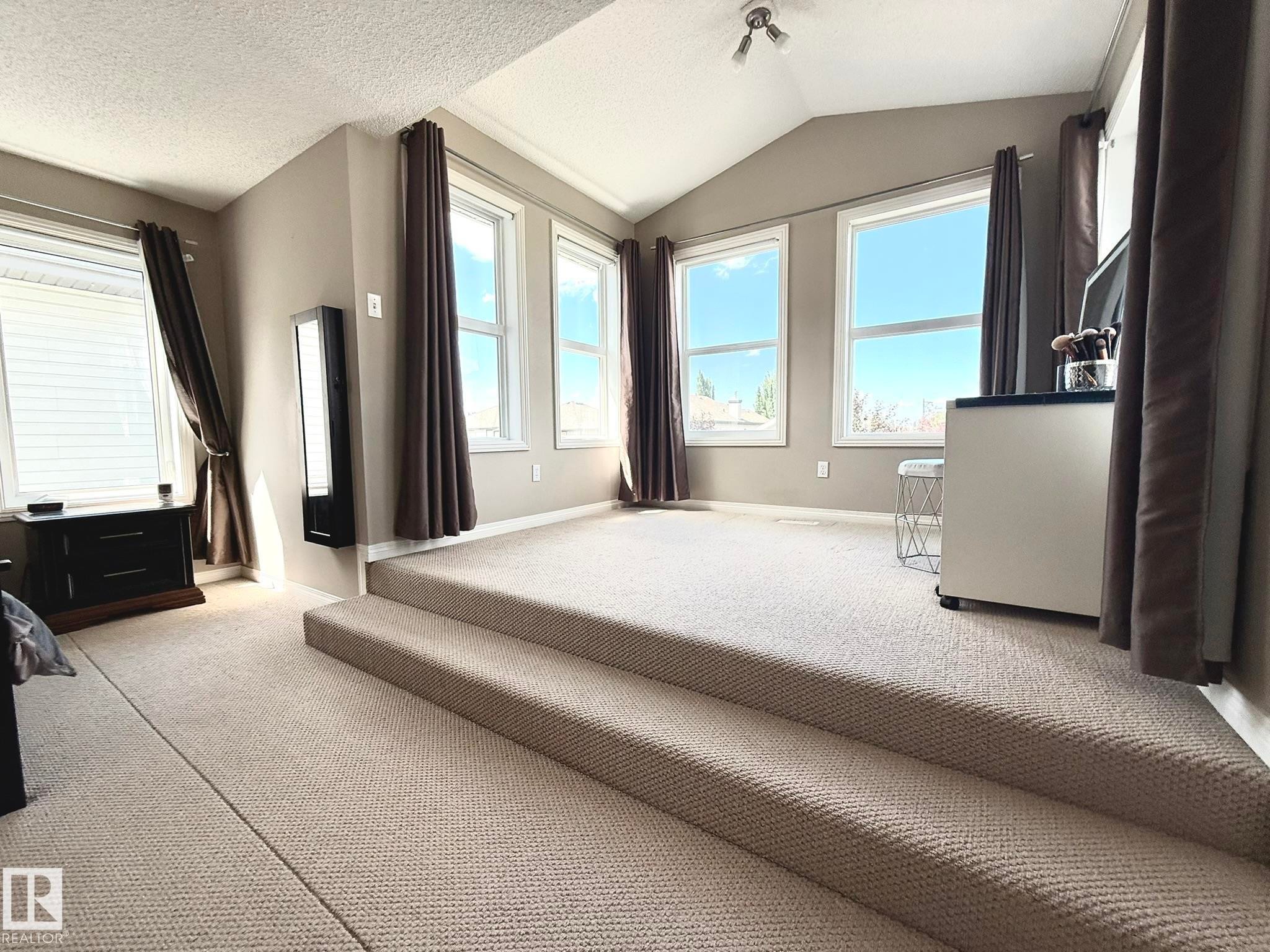 Multi-level room featuring neutral-toned carpeting, ample natural light from multiple windows, a vaulted ceiling, and recessed lighting - 1820 Robertson Crescent Sw, Edmonton, AB - Indoor