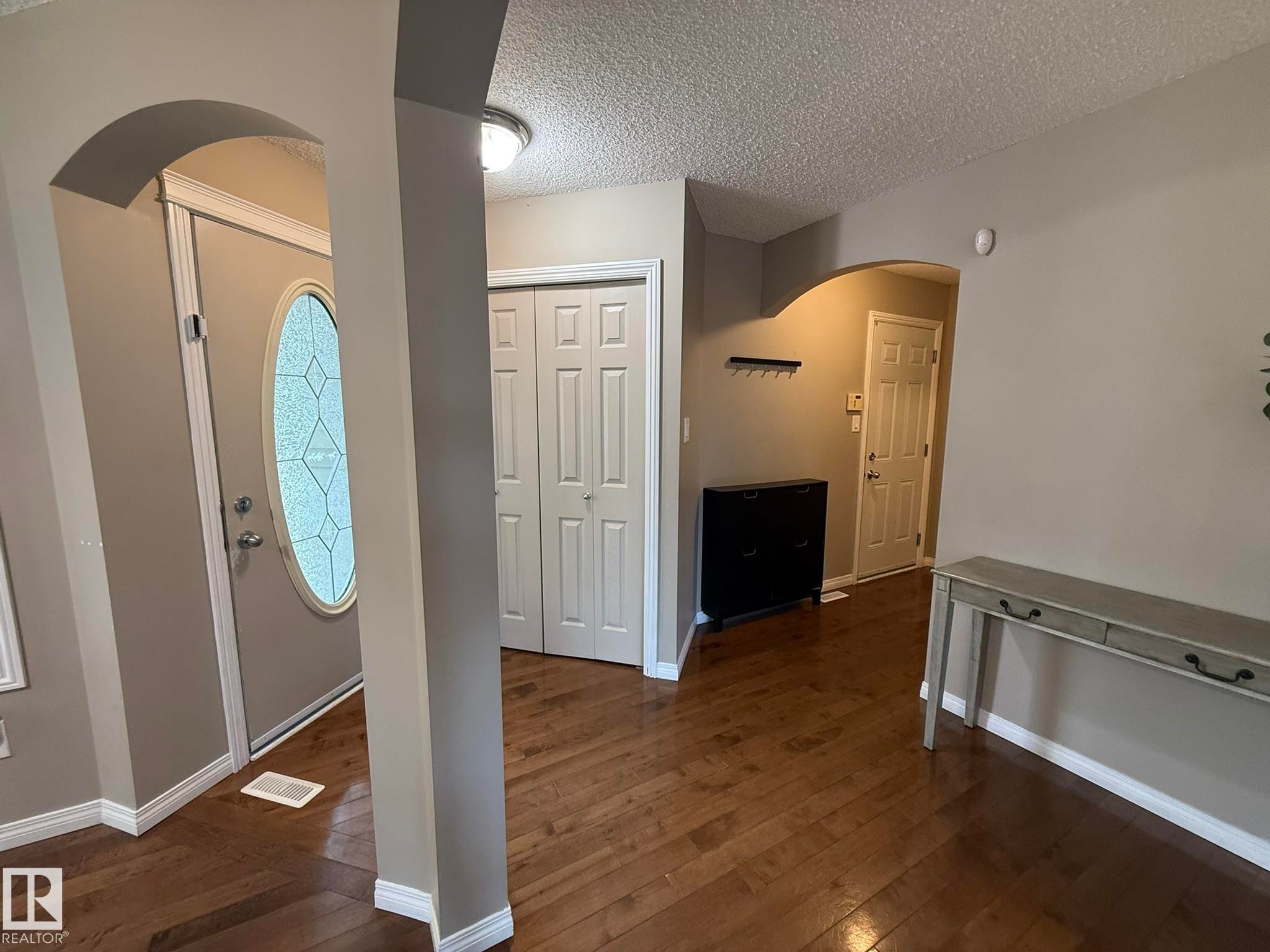 Arched doorway entryway featuring wood-finish flooring, a front door with an oval decorative glass insert, and bi-fold closet doors - 1820 Robertson Crescent Sw, Edmonton, AB - Indoor Photo Showing Other Room