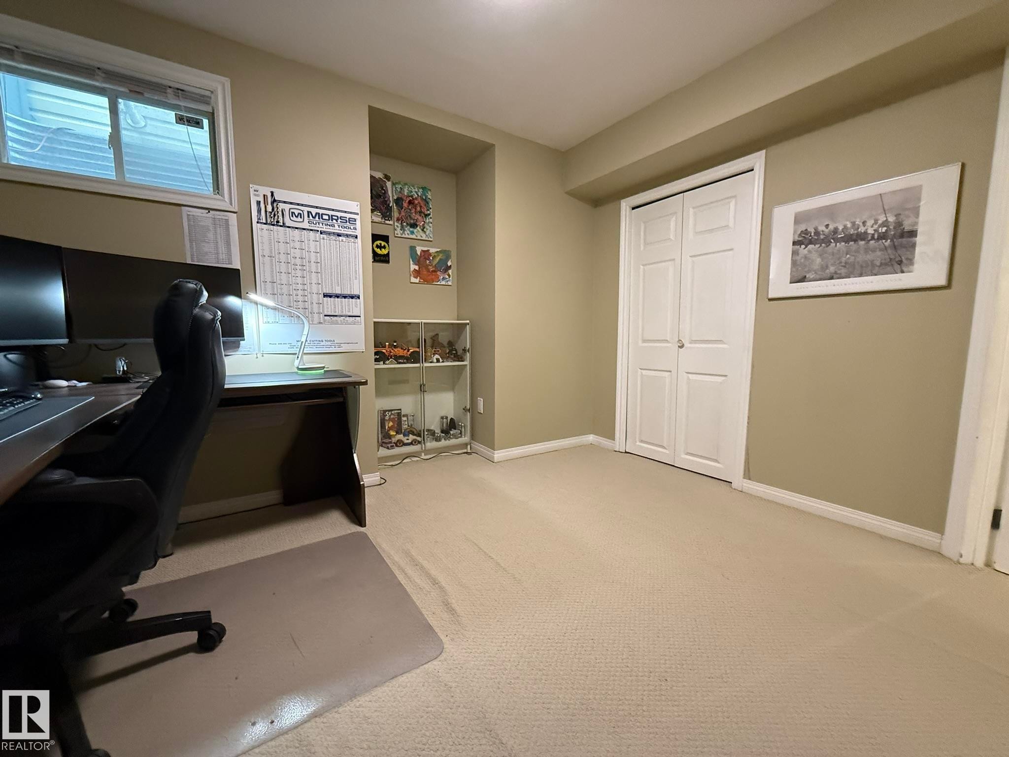 Carpeted room with a built-in closet featuring bi-fold doors, a recessed wall niche, and a window with blinds - 1820 Robertson Crescent Sw, Edmonton, AB - Indoor Photo Showing Office