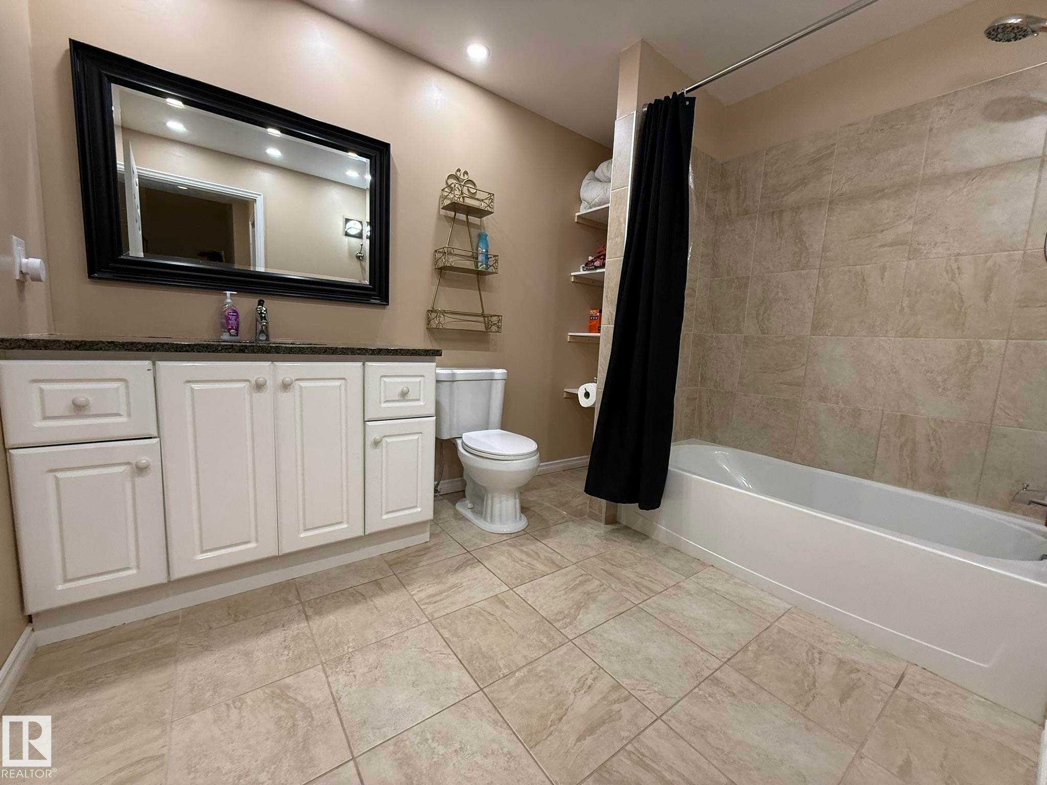Bathroom featuring a white vanity with a dark countertop, an expansive framed mirror, a tub/shower combination with tile surround, and tile flooring - 1820 Robertson Crescent Sw, Edmonton, AB - Indoor Photo Showing Bathroom
