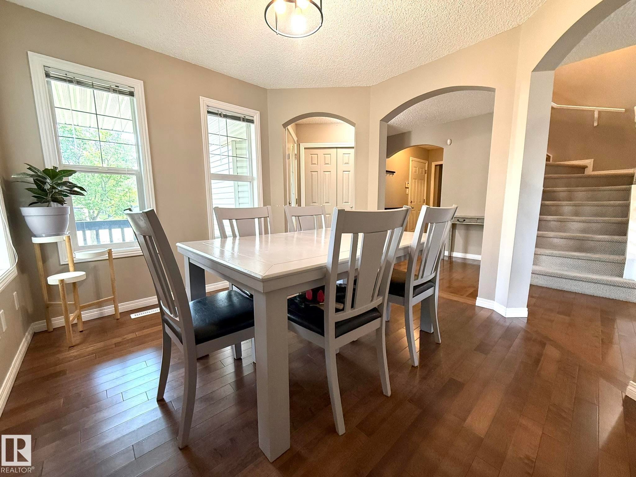 Spacious room featuring wood-finish flooring, multiple windows, and arched doorways - 1820 Robertson Crescent Sw, Edmonton, AB - Indoor Photo Showing Dining Room