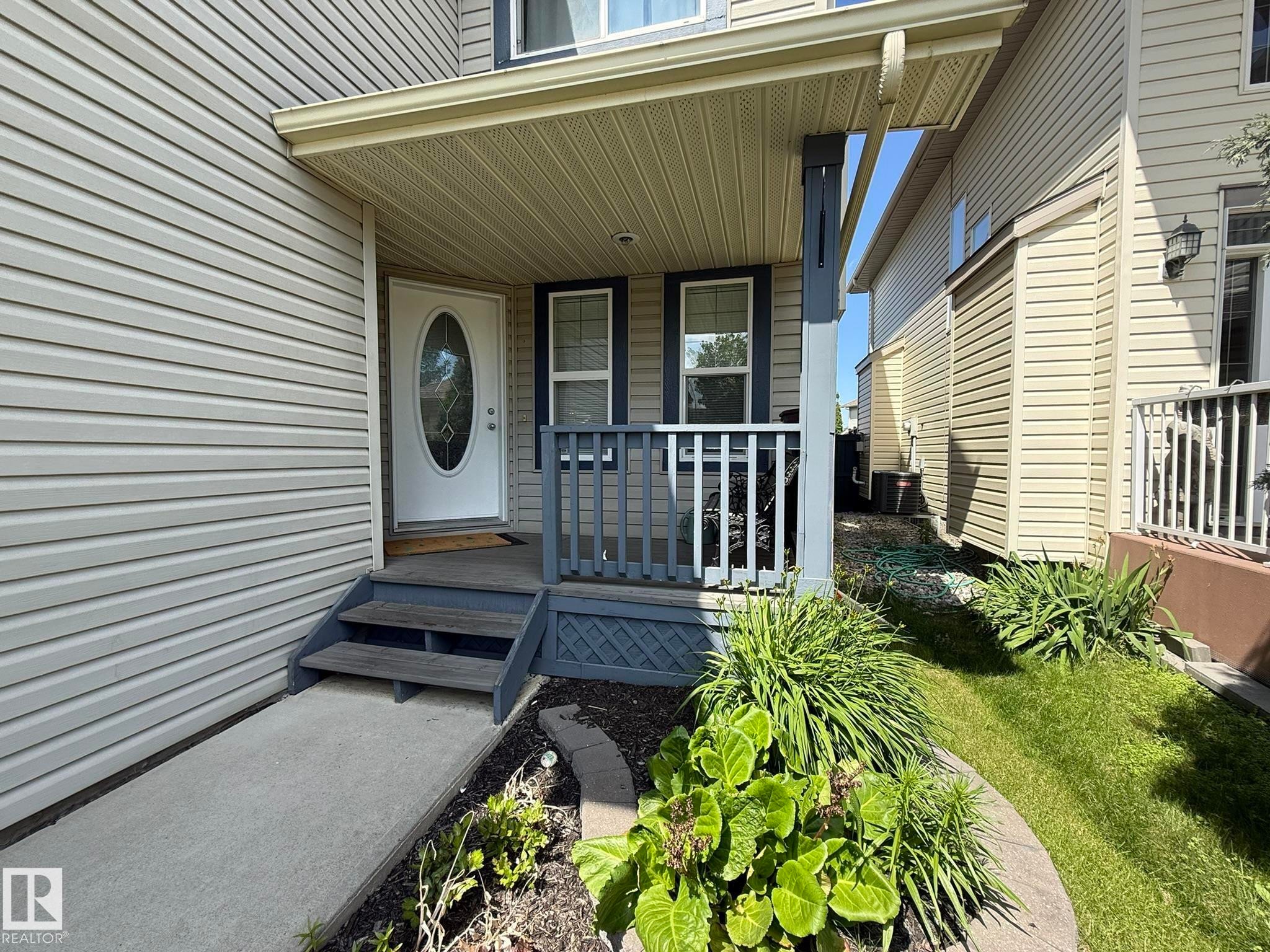 Covered front porch with a white oval-lite entry door, framed by dark blue trim and siding - 1820 Robertson Crescent Sw, Edmonton, AB - Outdoor With Deck Patio Veranda With Exterior