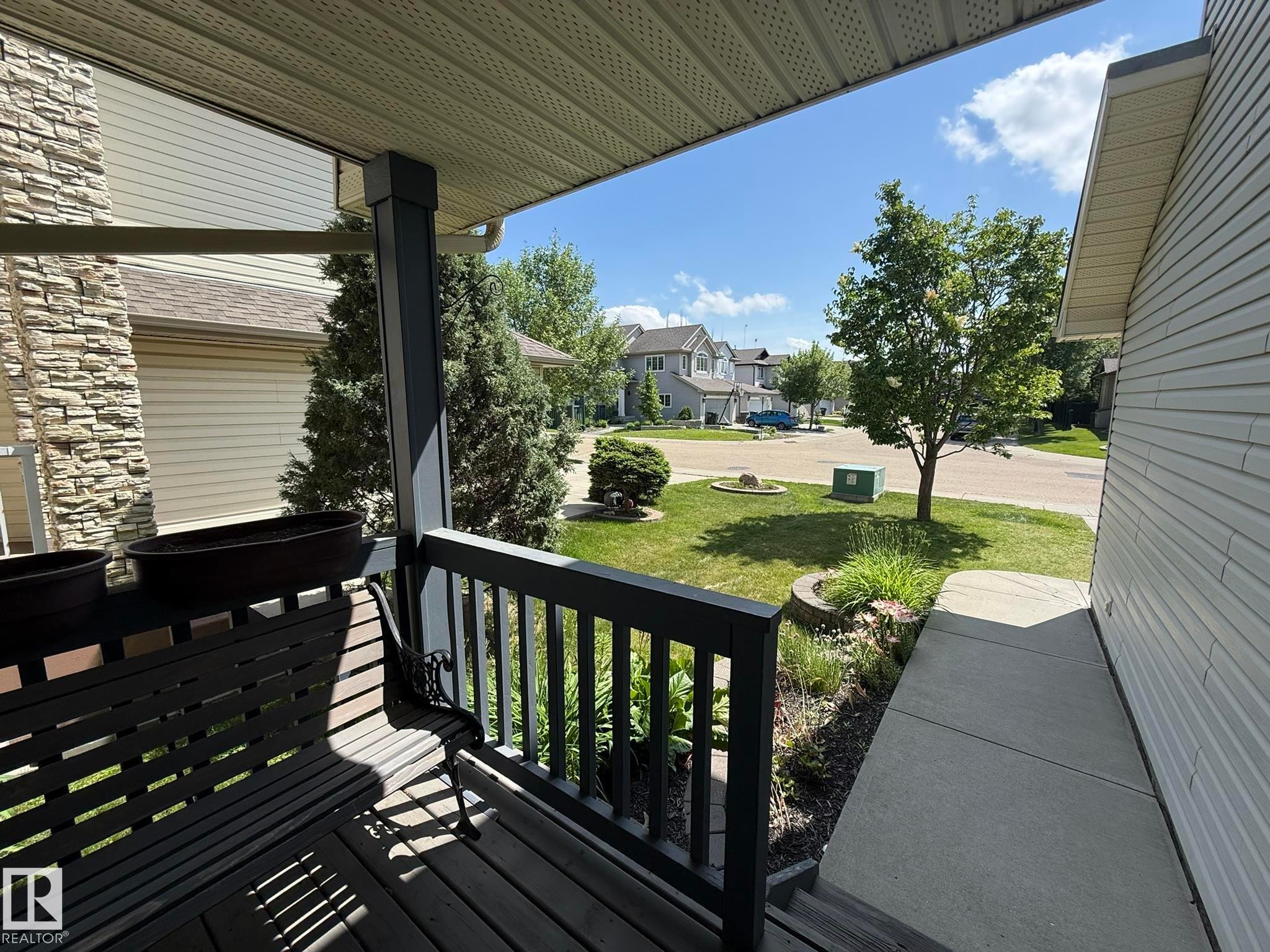 Inviting front porch featuring a dark wood deck, coordinating railings, and a slatted porch swing - 1820 Robertson Crescent Sw, Edmonton, AB - Outdoor With Deck Patio Veranda With Exterior