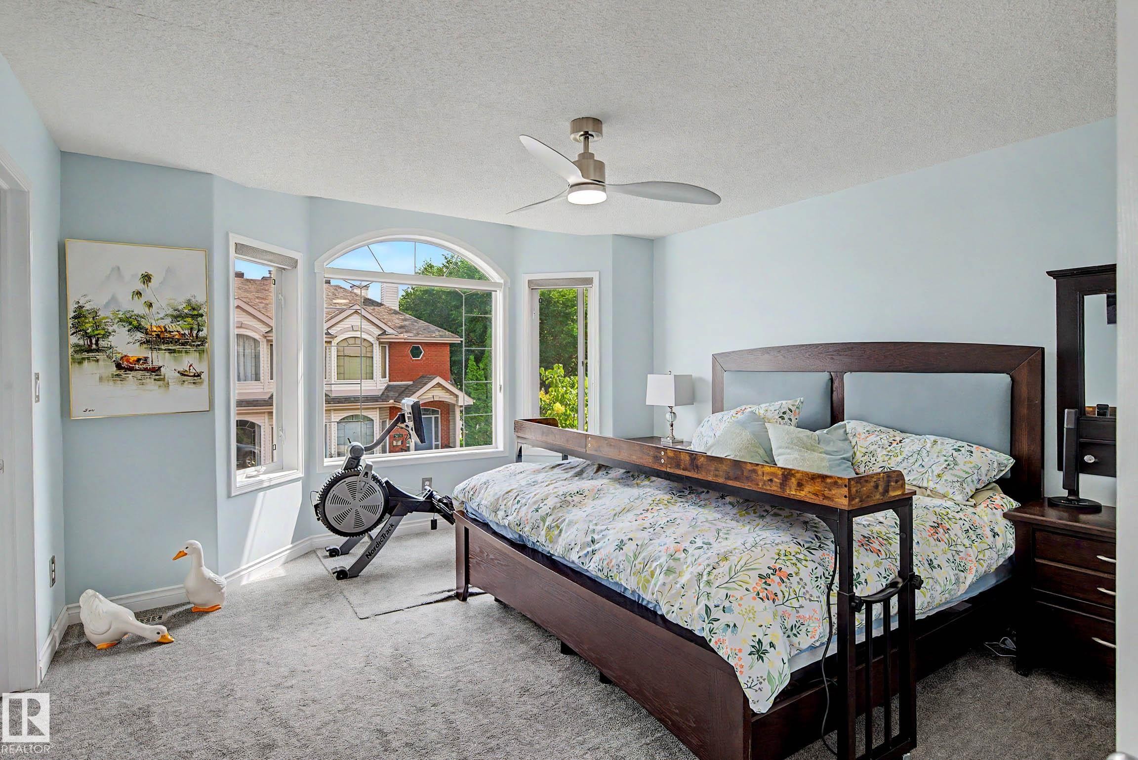 Spacious bedroom featuring multiple windows, including an arched window, and light blue walls - 9130 100A Avenue Nw, Edmonton, AB - Indoor Photo Showing Bedroom