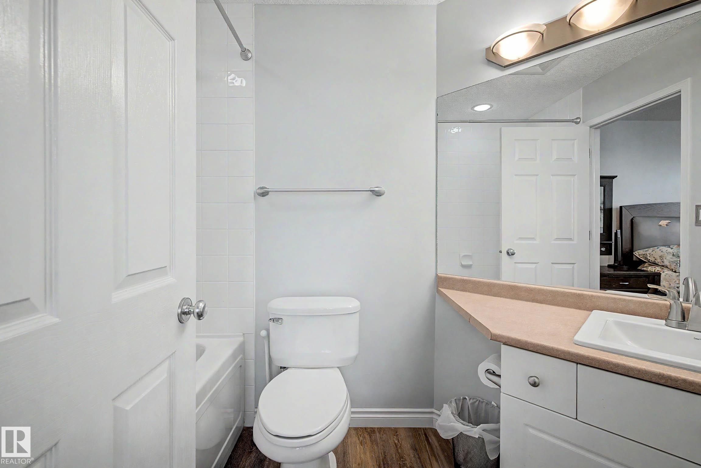 Full bathroom featuring a single vanity with an integrated sink, a large wall-mounted mirror, a toilet, and a shower-over-tub combination with white subway tile surround - 9130 100A Avenue Nw, Edmonton, AB - Indoor Photo Showing Bathroom